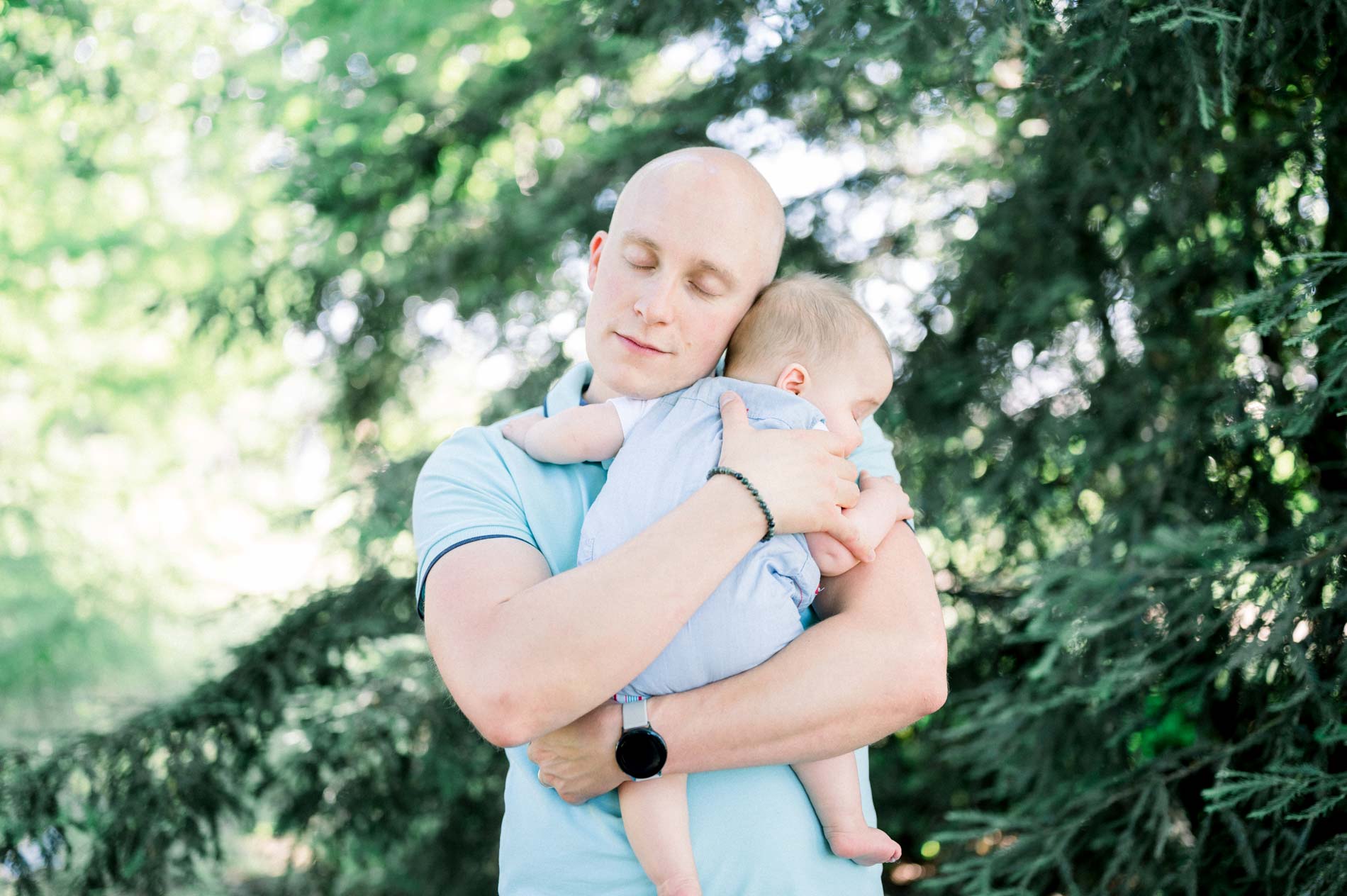 Dad holding his baby tenderly close in the greenery