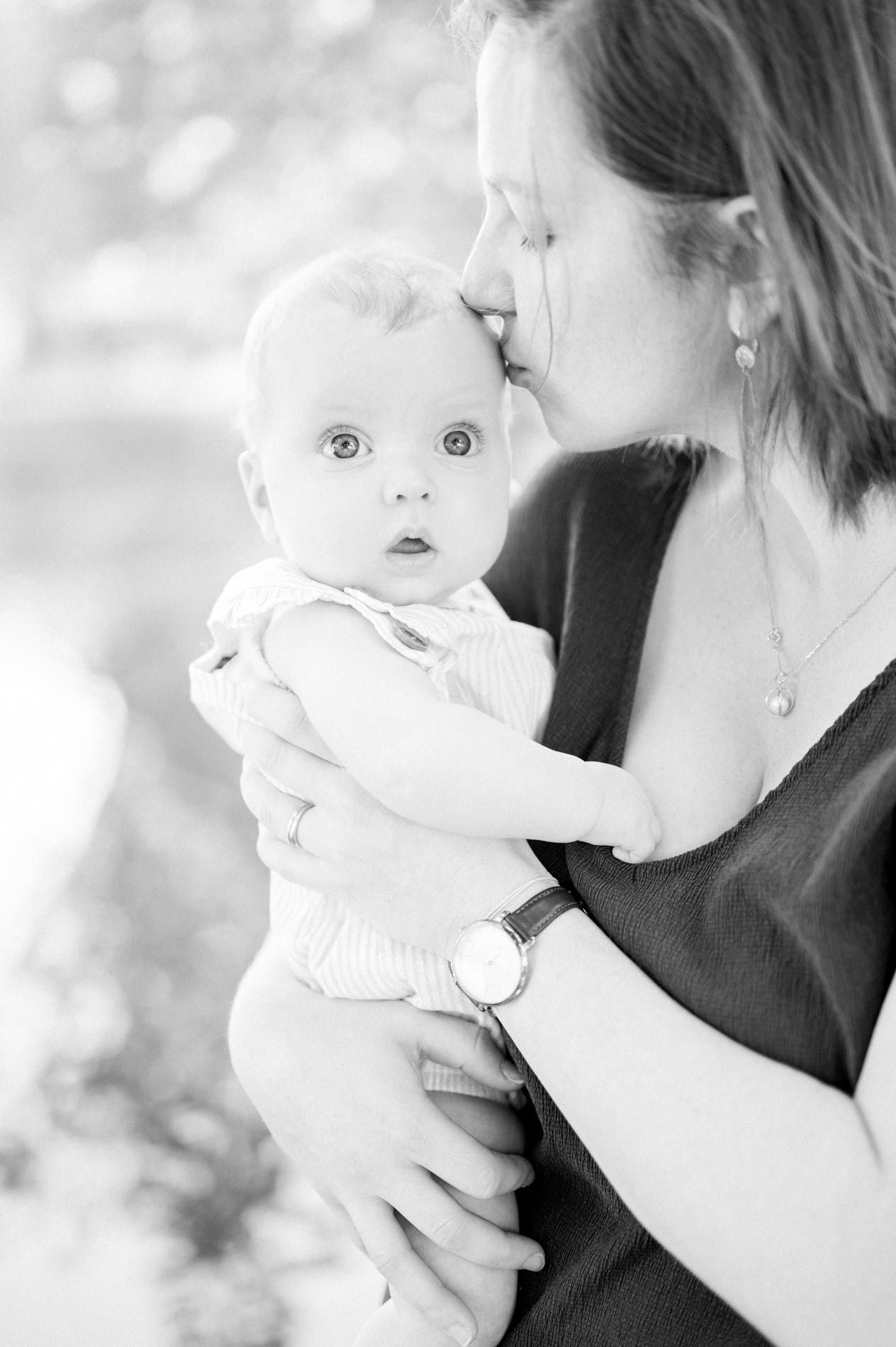 Mum kissing her baby who looks at the camera, in black and white