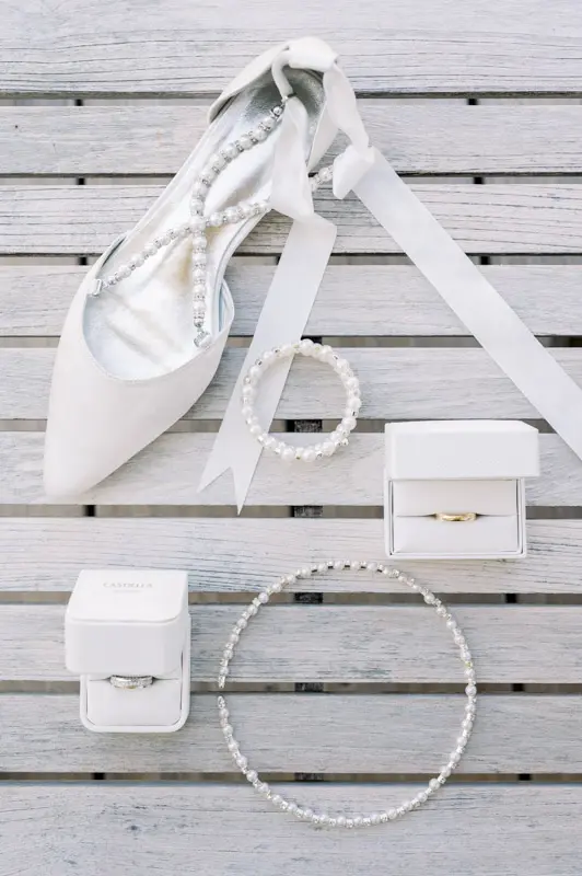 Bridal shoes, pearl jewellery and ring boxes laid out on white wooden boards