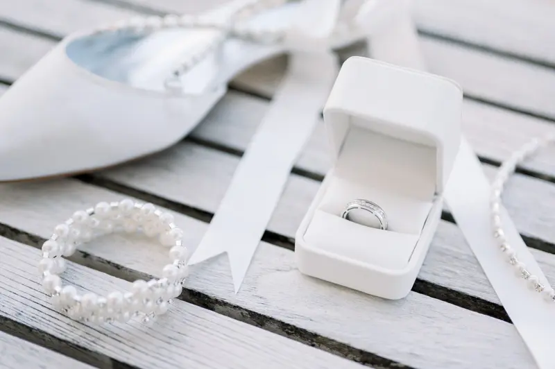 Wedding bands in a white box beside a pearl bracelet and a bridal shoe