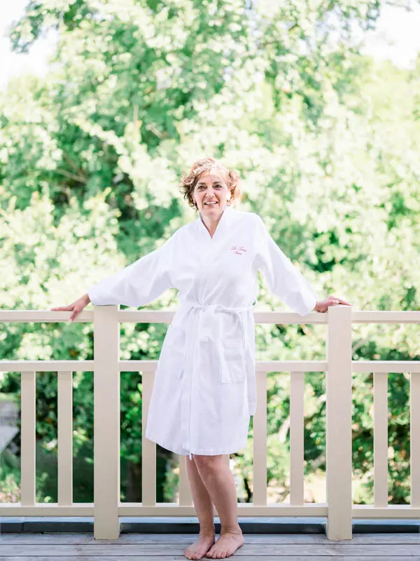 The bride in a white robe smiling on the balcony while getting ready