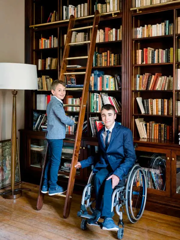 The couple's children in suits posing in front of the library bookshelves