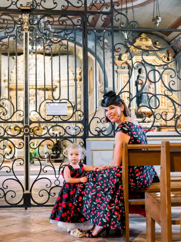 Guest and little girl in floral dresses seated by the church's wrought-iron gate