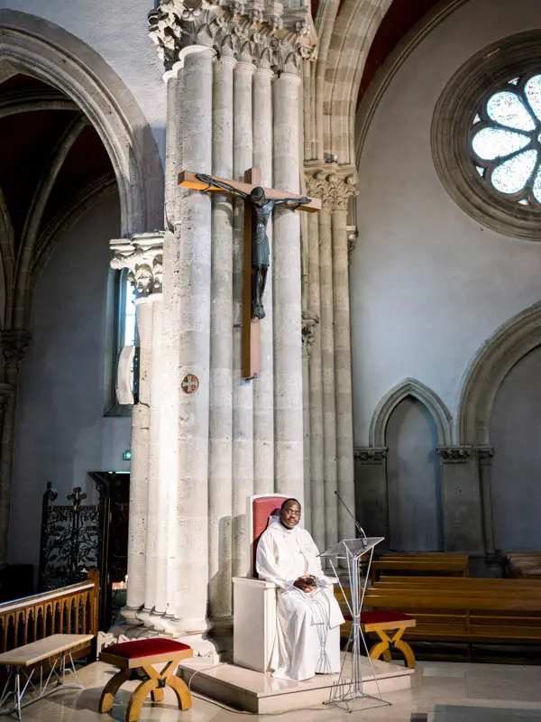 The priest seated near the altar beneath the crucifix during the religious ceremony