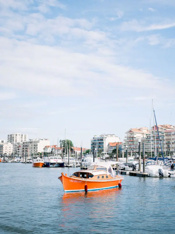 Small orange boat crossing Arcachon harbour in front of the seafront buildings