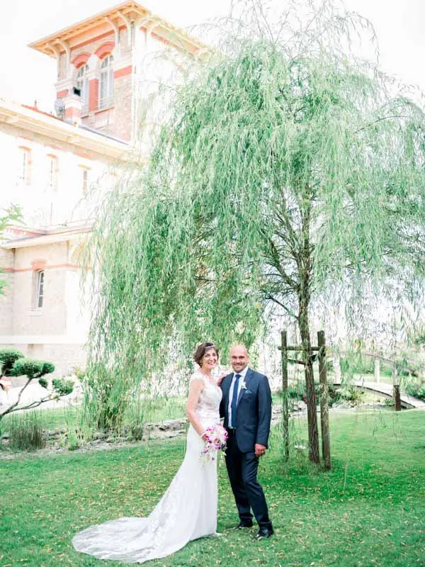The bride and groom pose beneath a weeping willow in the Villa La Tosca garden