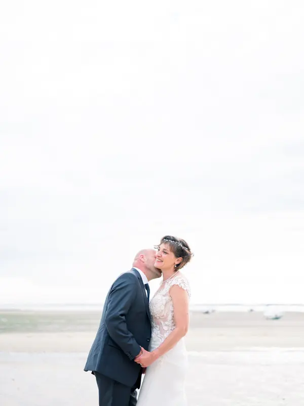 The newlyweds kiss on the beach at Arcachon Bay in soft, milky light