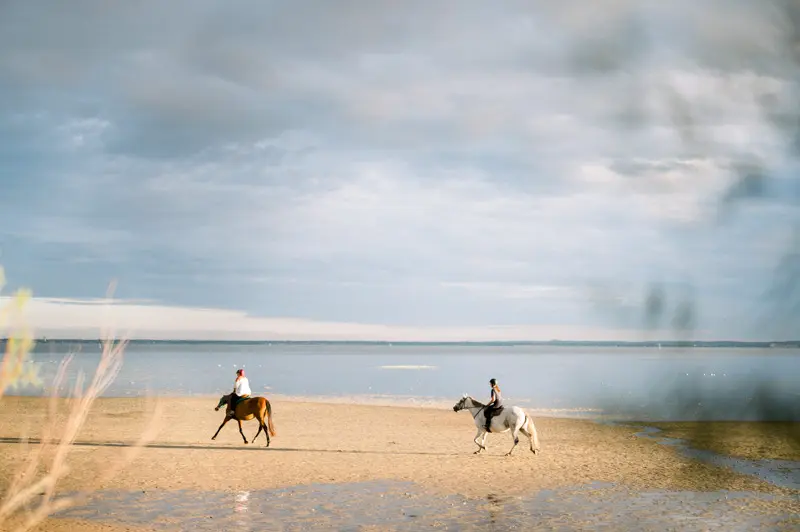 Two riders on horseback along the beach at Arcachon Bay in the evening