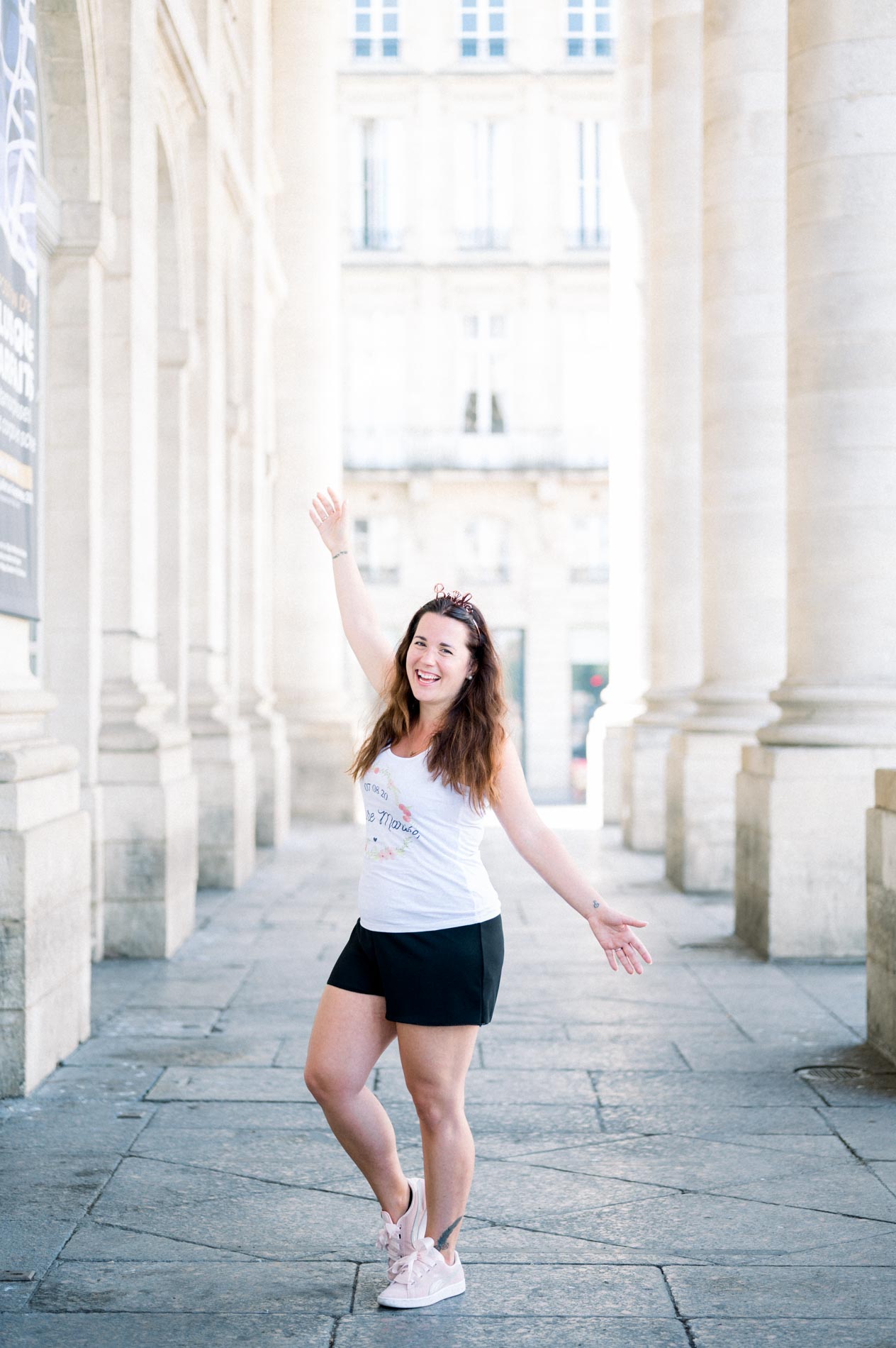 The bride-to-be raising an arm joyfully under the colonnade at her hen party