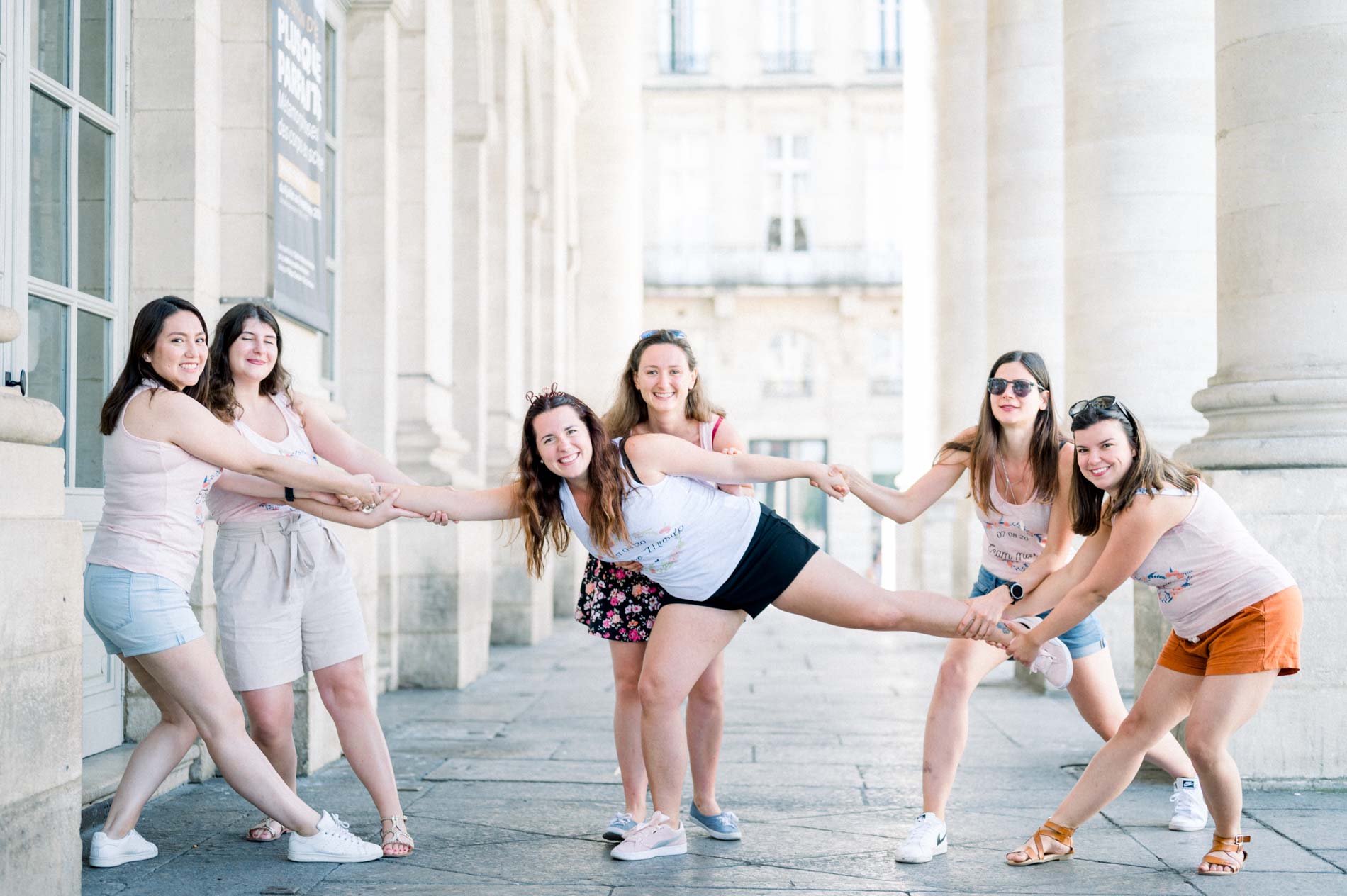 Friends playfully pulling the bride-to-be by the arms under the colonnade