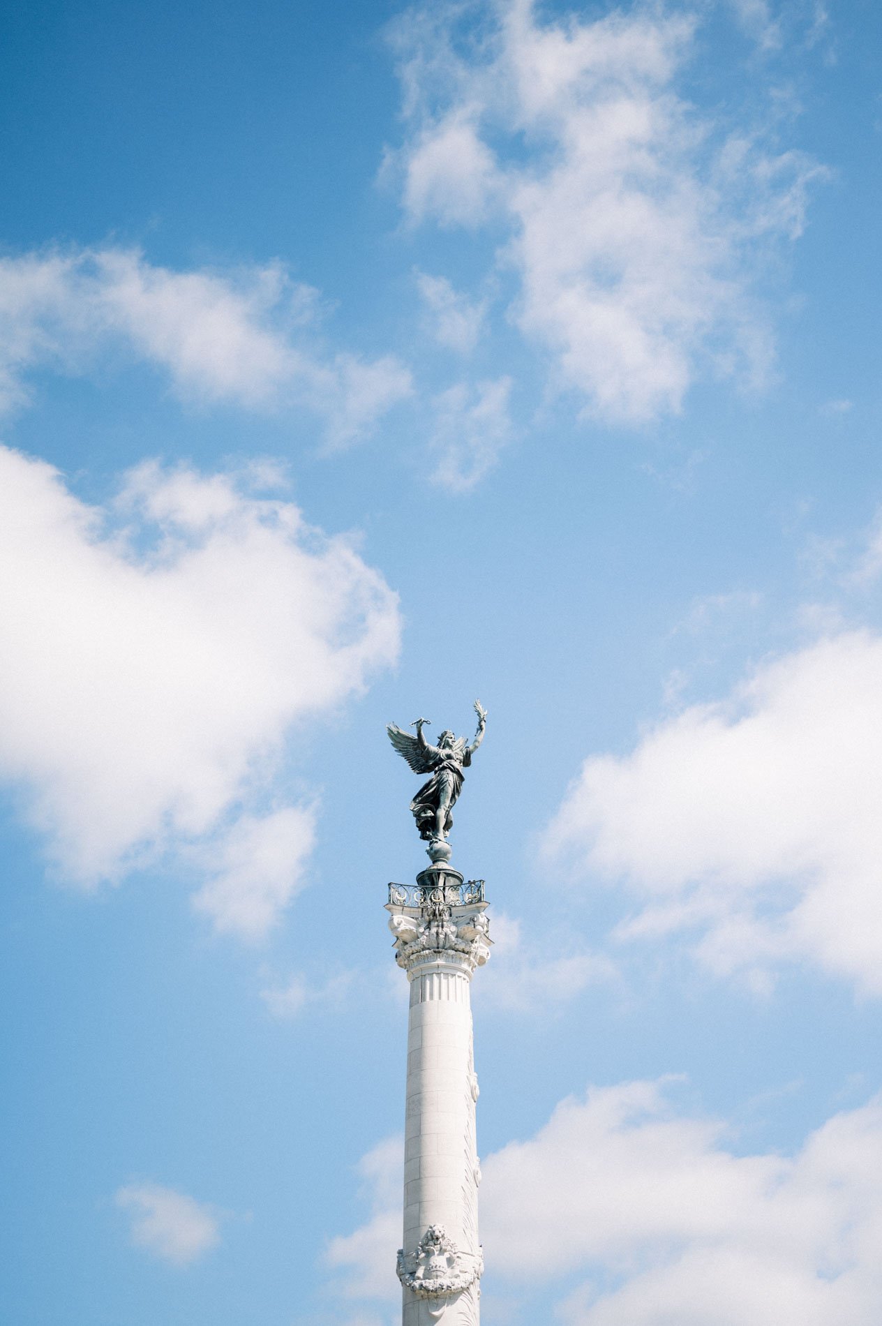 The tall Girondins column and its statue rising into a cloudy blue sky