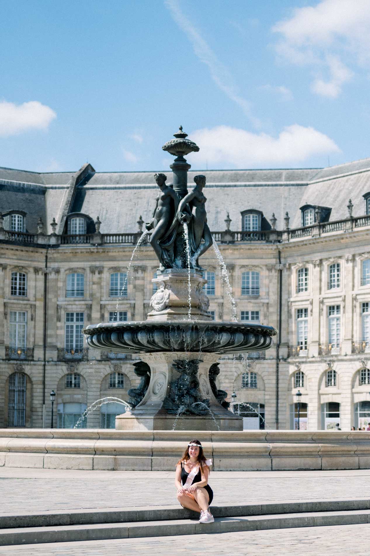 The bride-to-be sitting at the foot of a large fountain facing the Bourse building