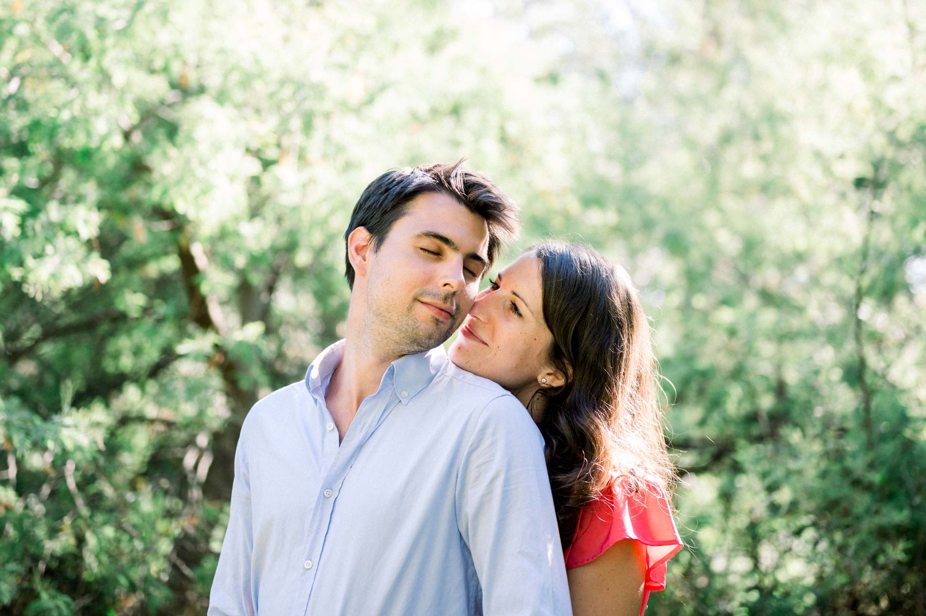The bride-to-be rests her head on her fiancé's shoulder amid the greenery