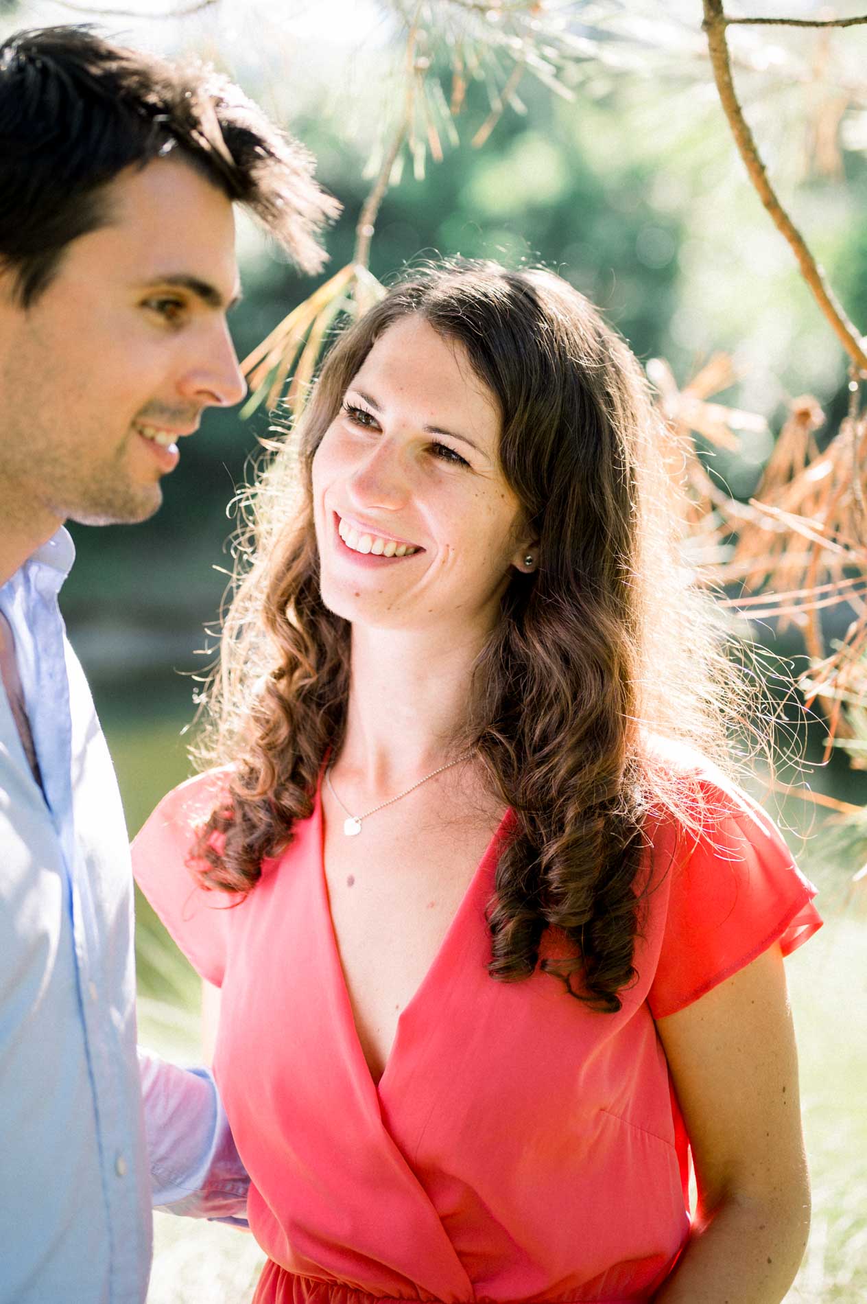 The engaged couple exchange a knowing look beneath the pine branches