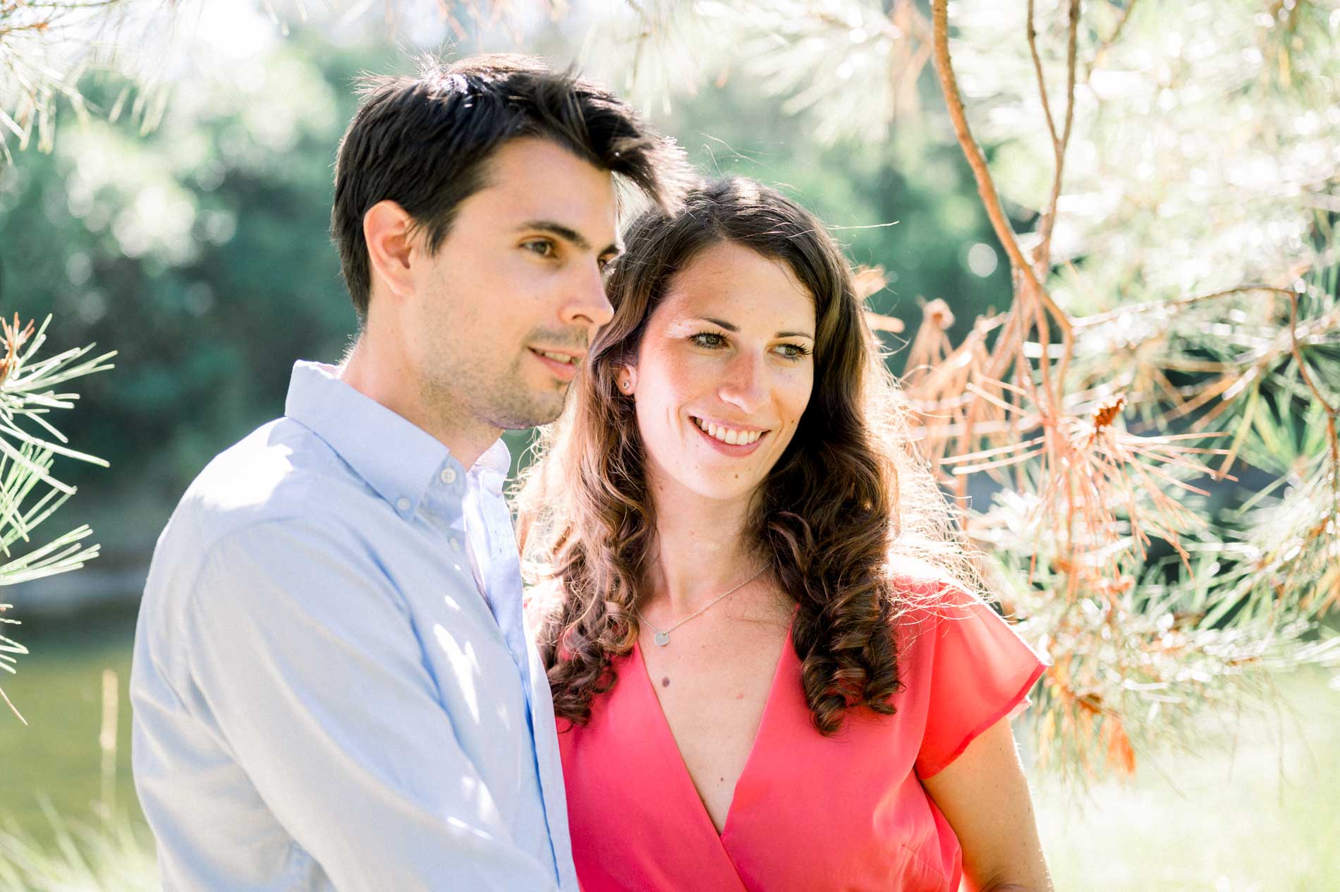 The couple smiling side by side by the water during their engagement session