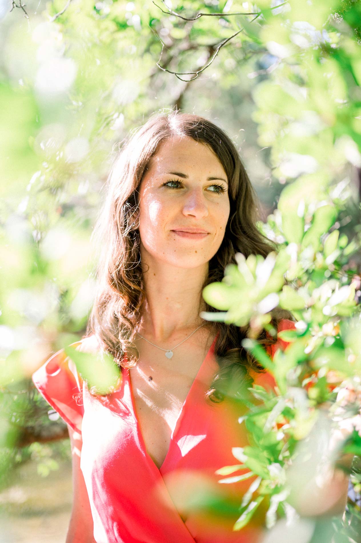 Portrait of the bride-to-be in a coral dress framed by foliage