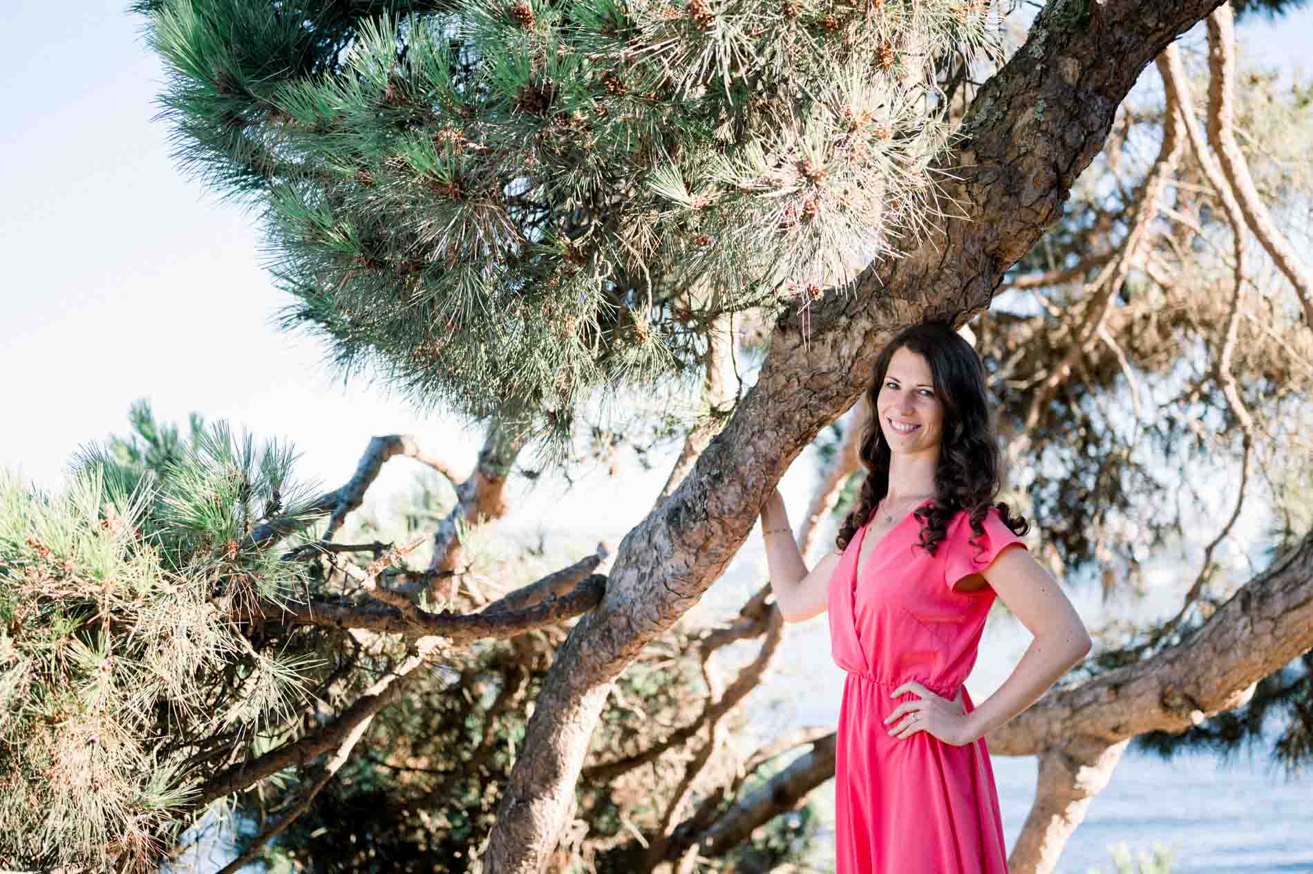 The bride-to-be leaning on a large pine branch facing the water