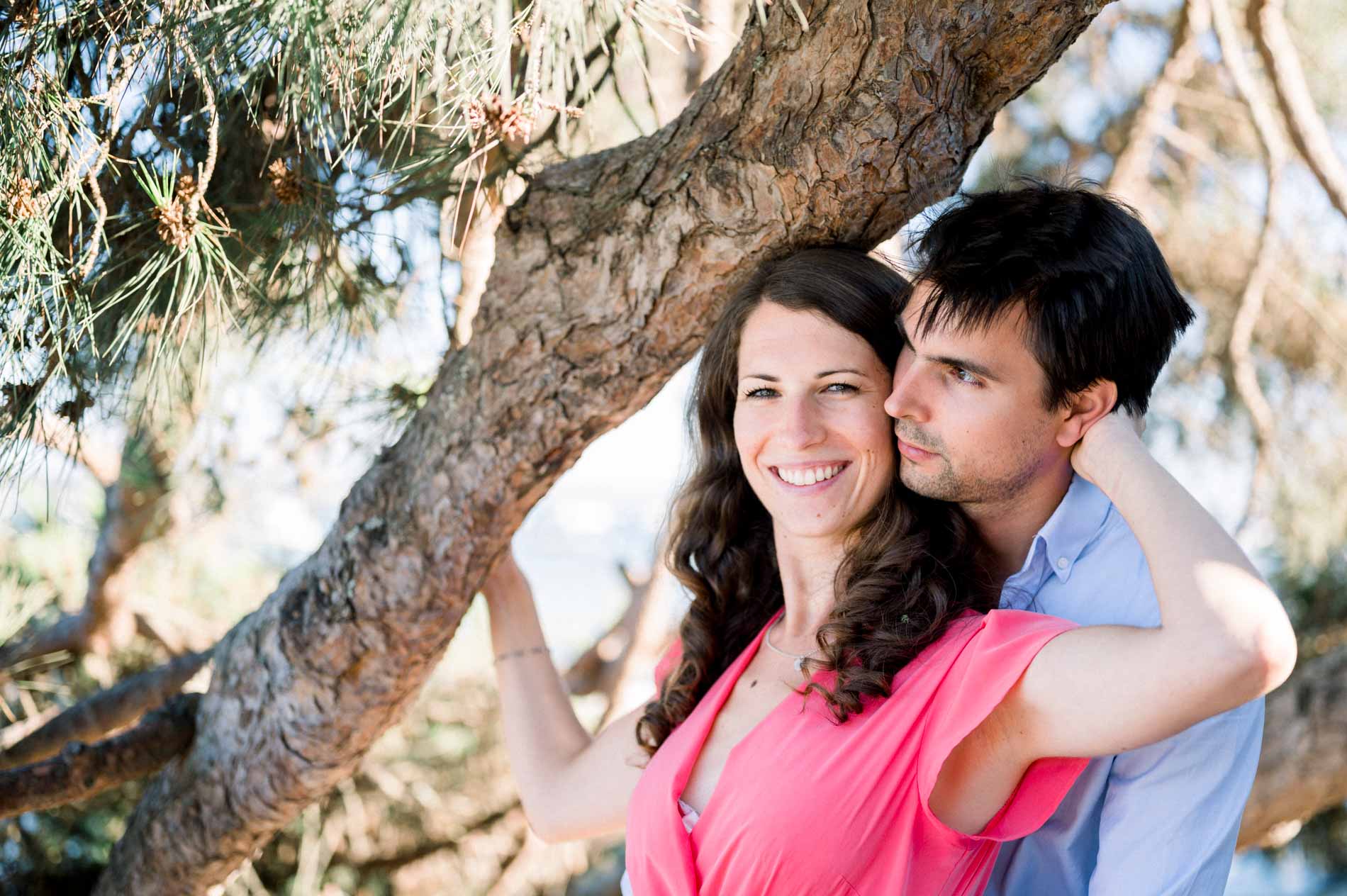 The couple laughing cheek to cheek under the branches of a pine