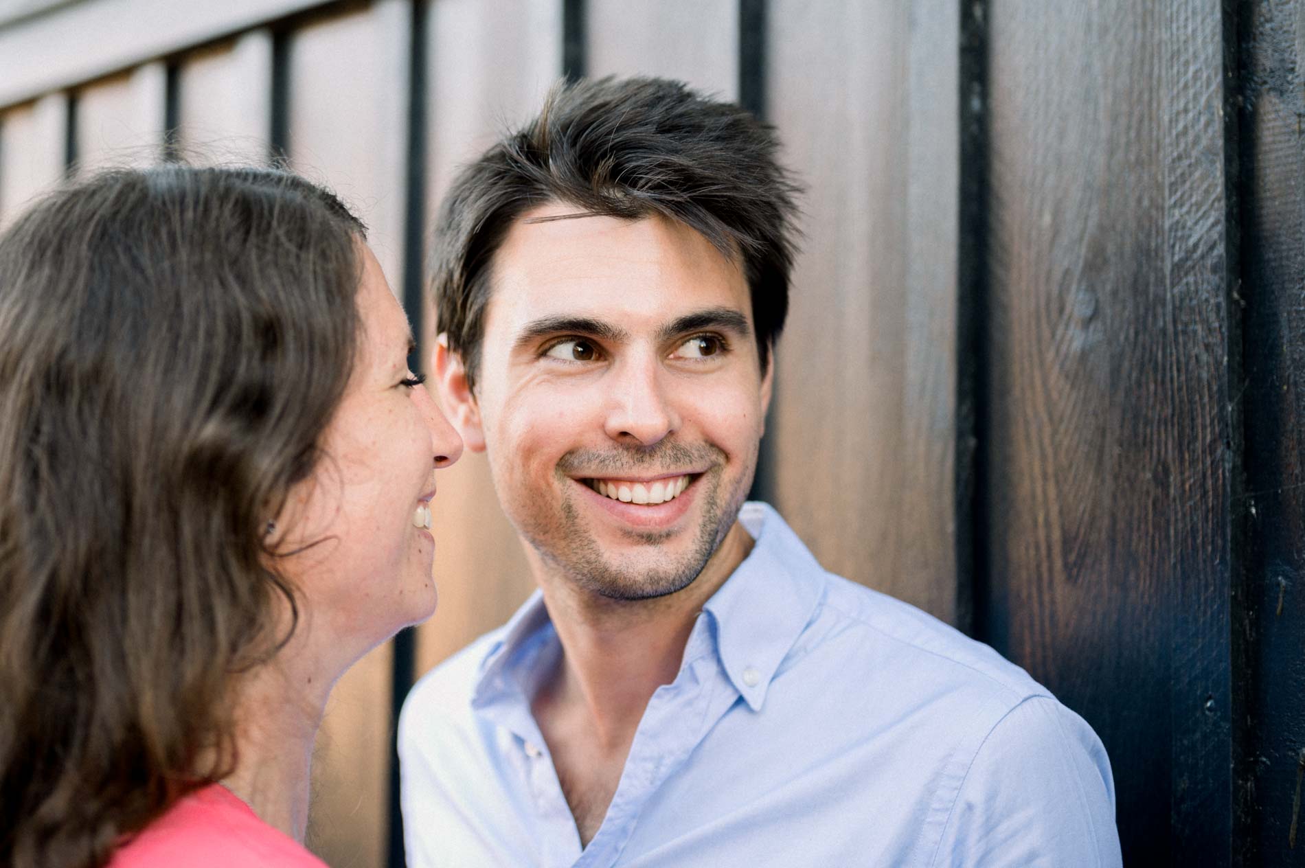 The fiancé smiles warmly at his bride-to-be in front of a wooden hut