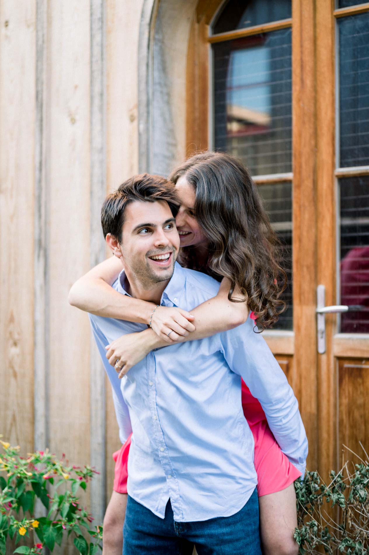 The fiancé gives his bride-to-be a piggyback in front of a wooden door