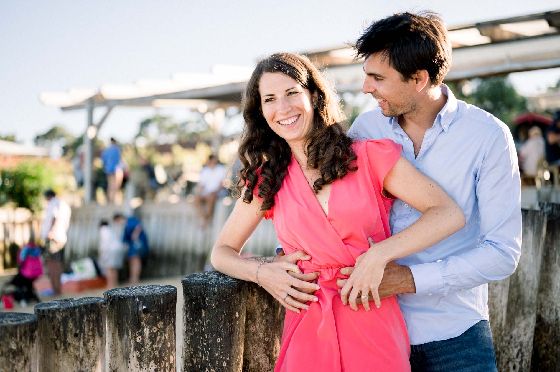 The engaged couple laughing together, leaning on a fence at the oyster harbour