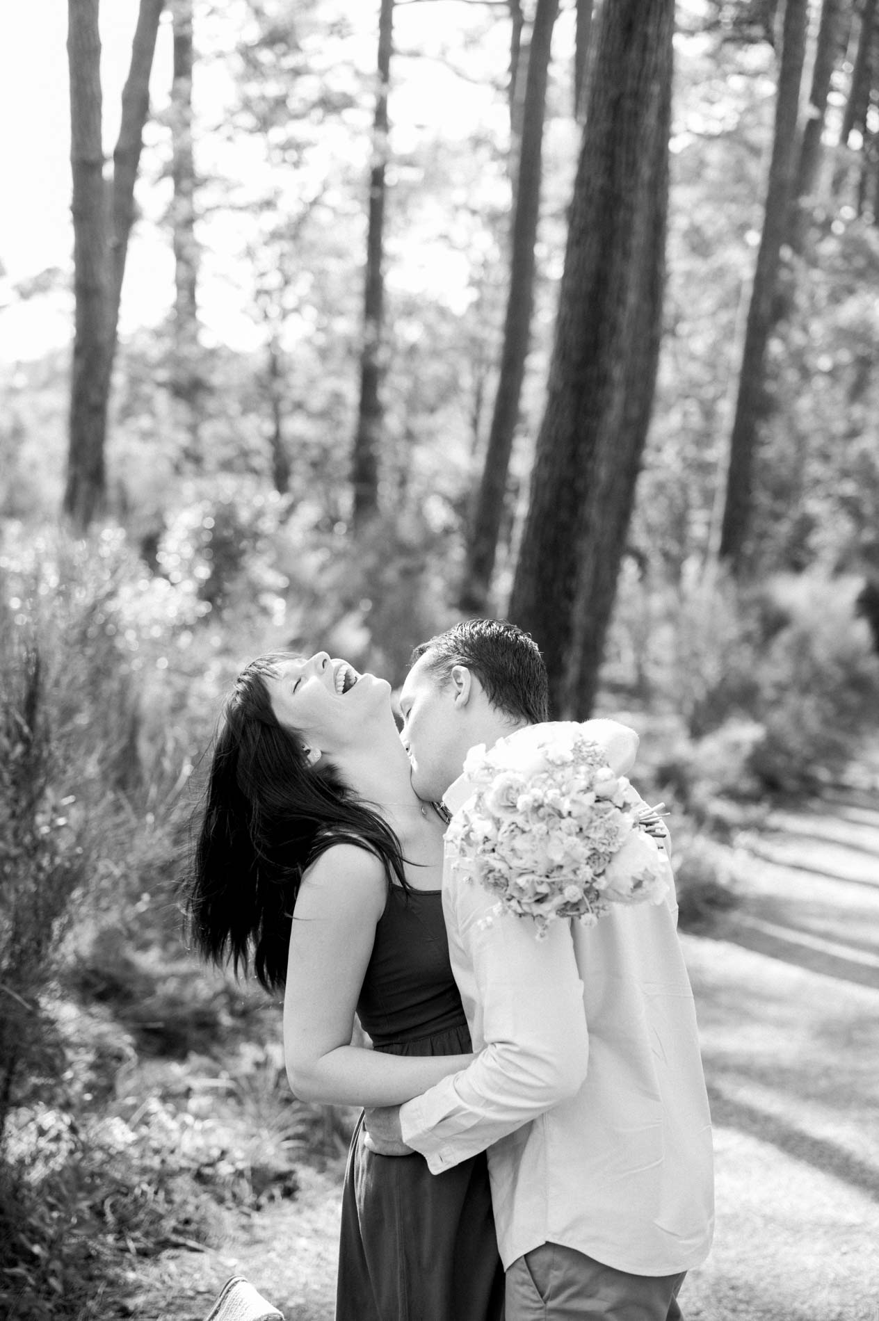 Black and white shot of the engaged couple kissing in the pine forest