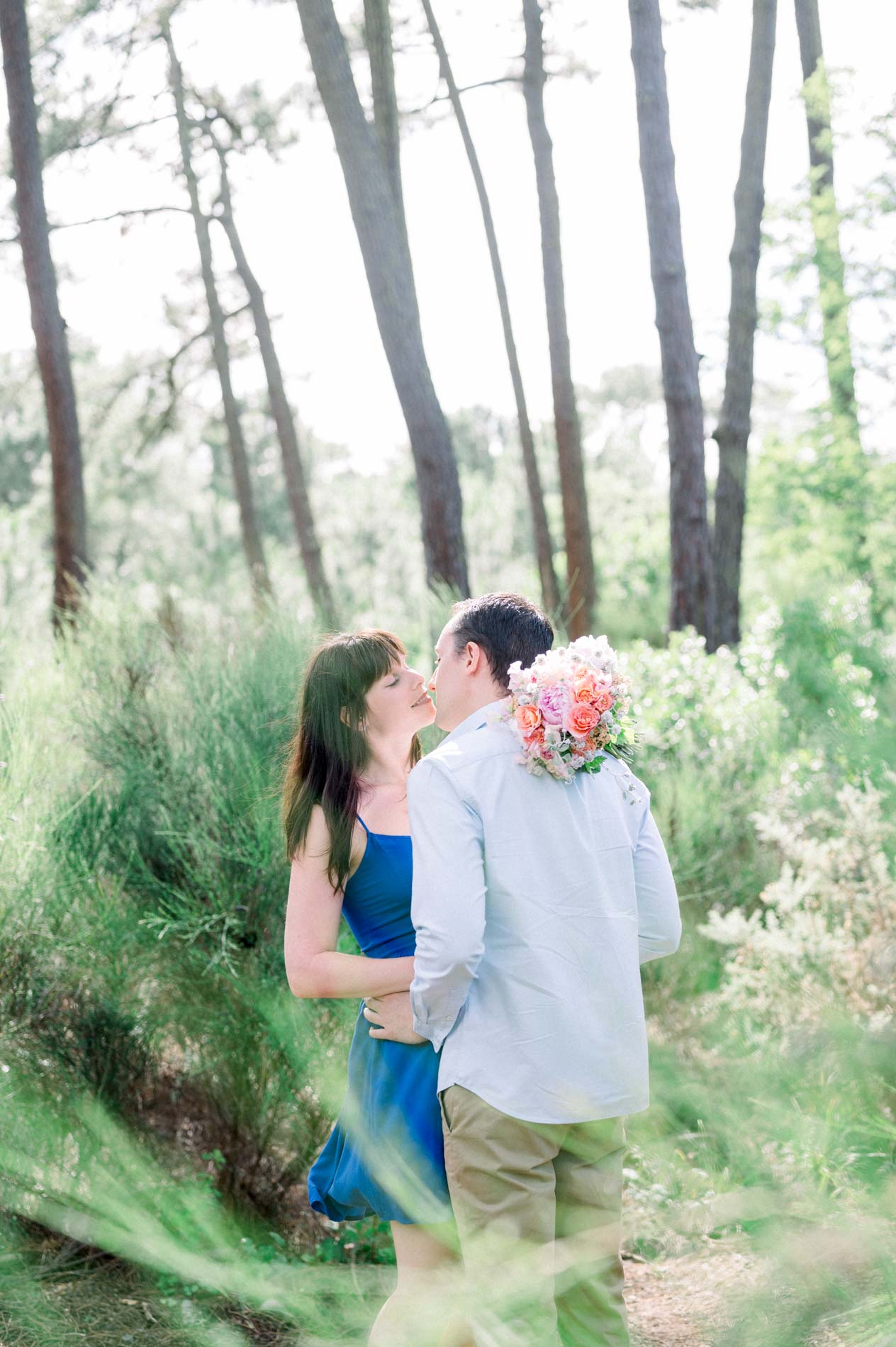 The couple embracing in tall grass among the pines during their engagement shoot