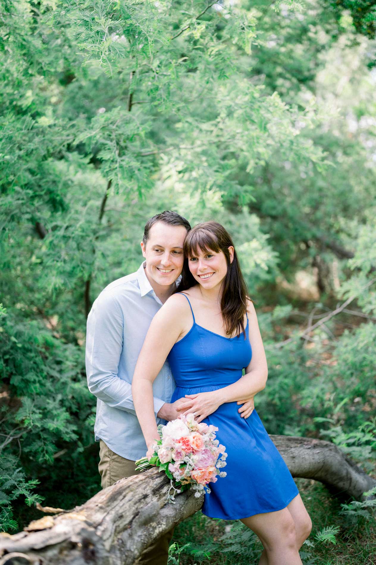 The couple sitting on a fallen trunk amid the greenery, holding a bouquet