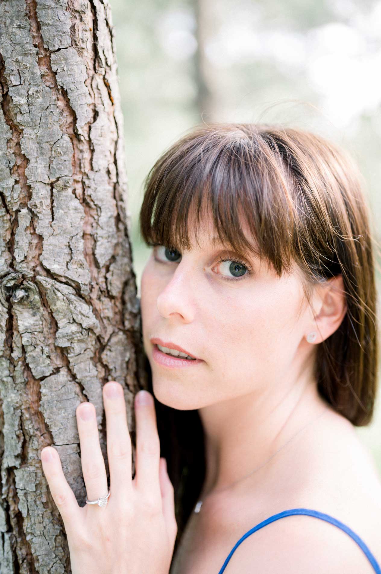 Close portrait of the bride-to-be, her cheek against the bark of a pine