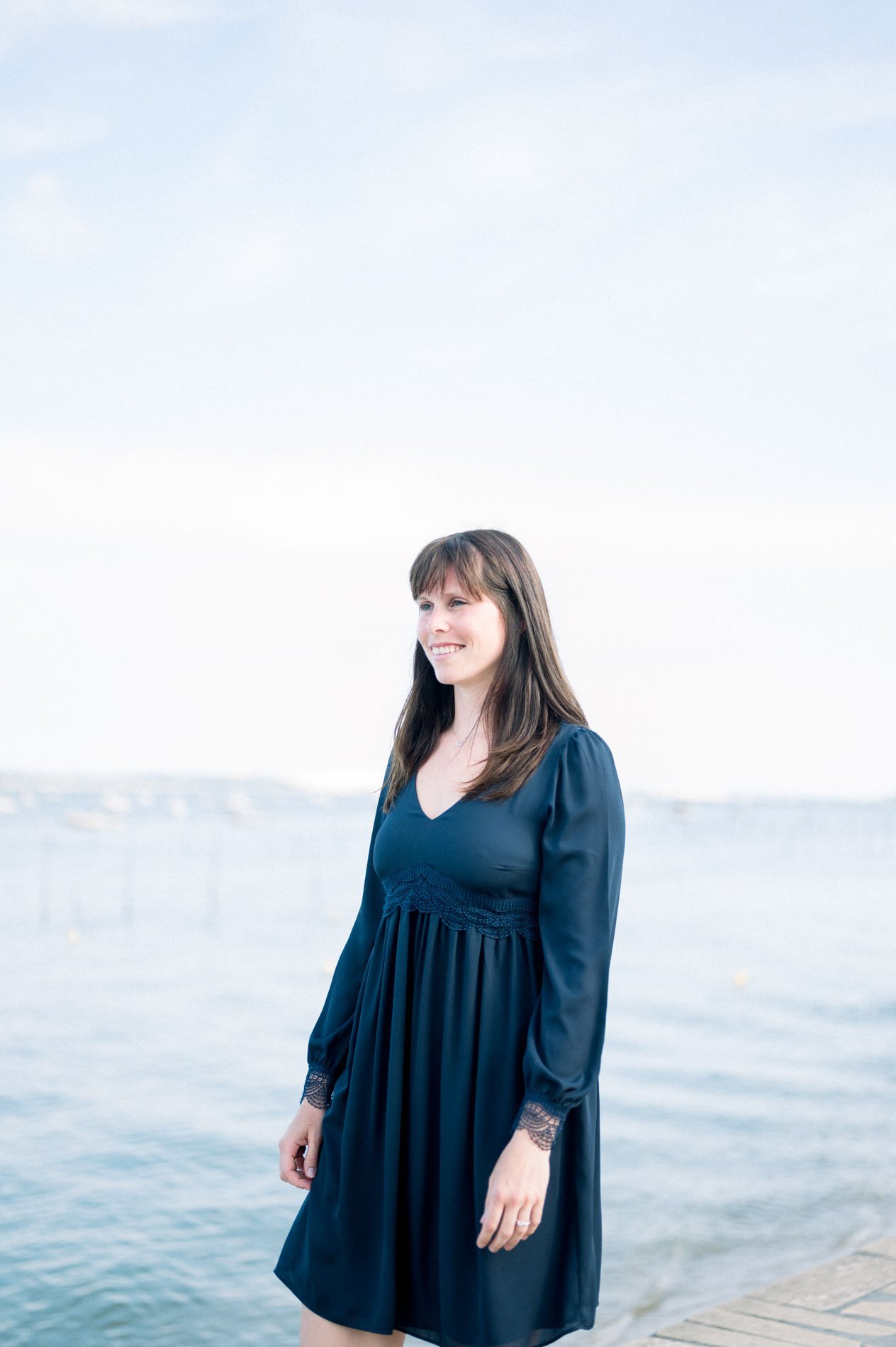 The bride-to-be in a navy dress by the bay in soft milky light