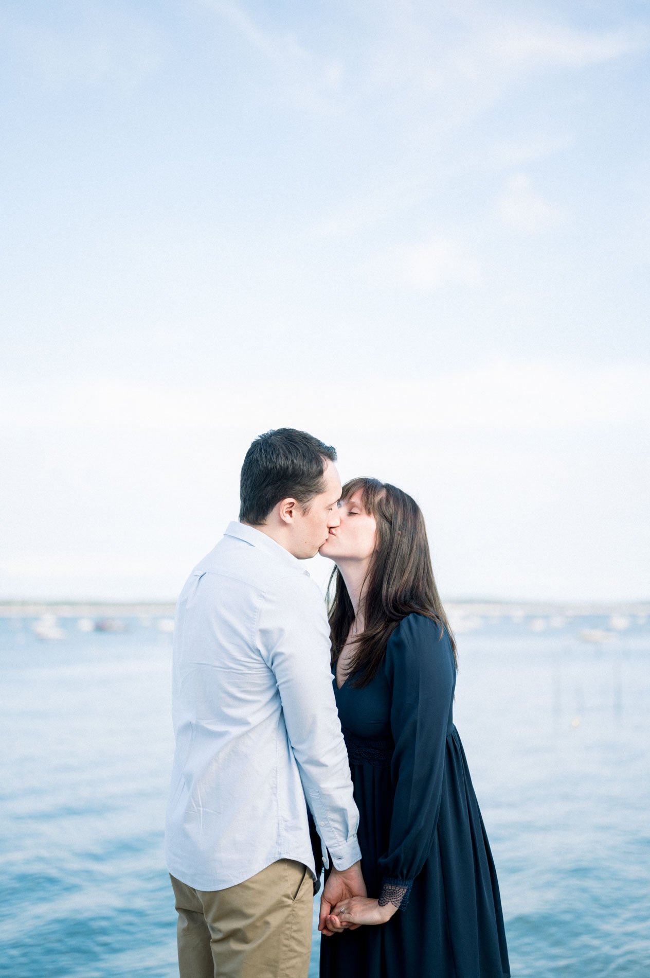 The engaged couple kiss on the shore of Arcachon Bay under a pale sky