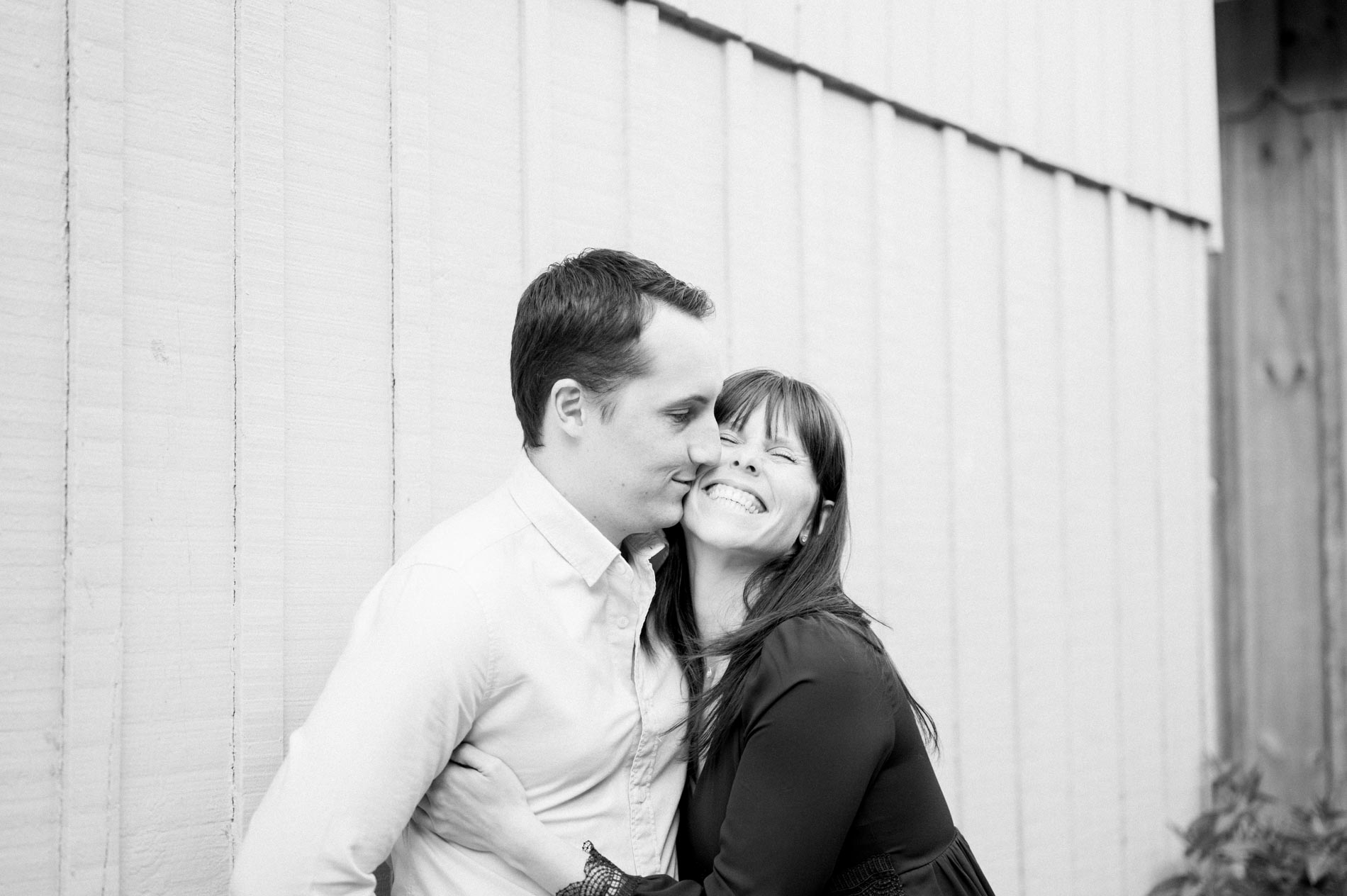 Black and white shot of the engaged couple cheek to cheek by a cabin
