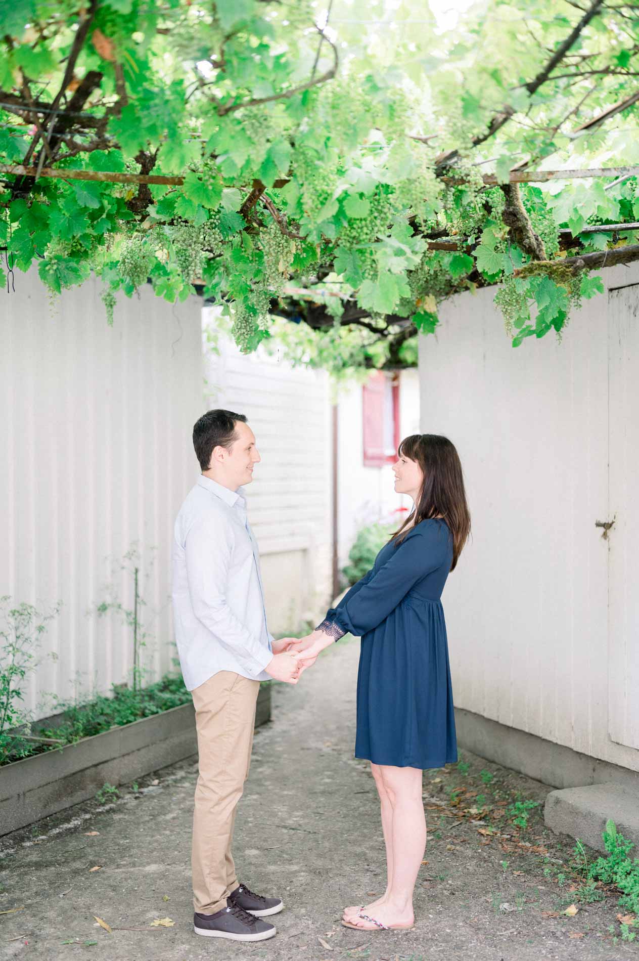 The couple holding hands in a lane beneath a grapevine arbour
