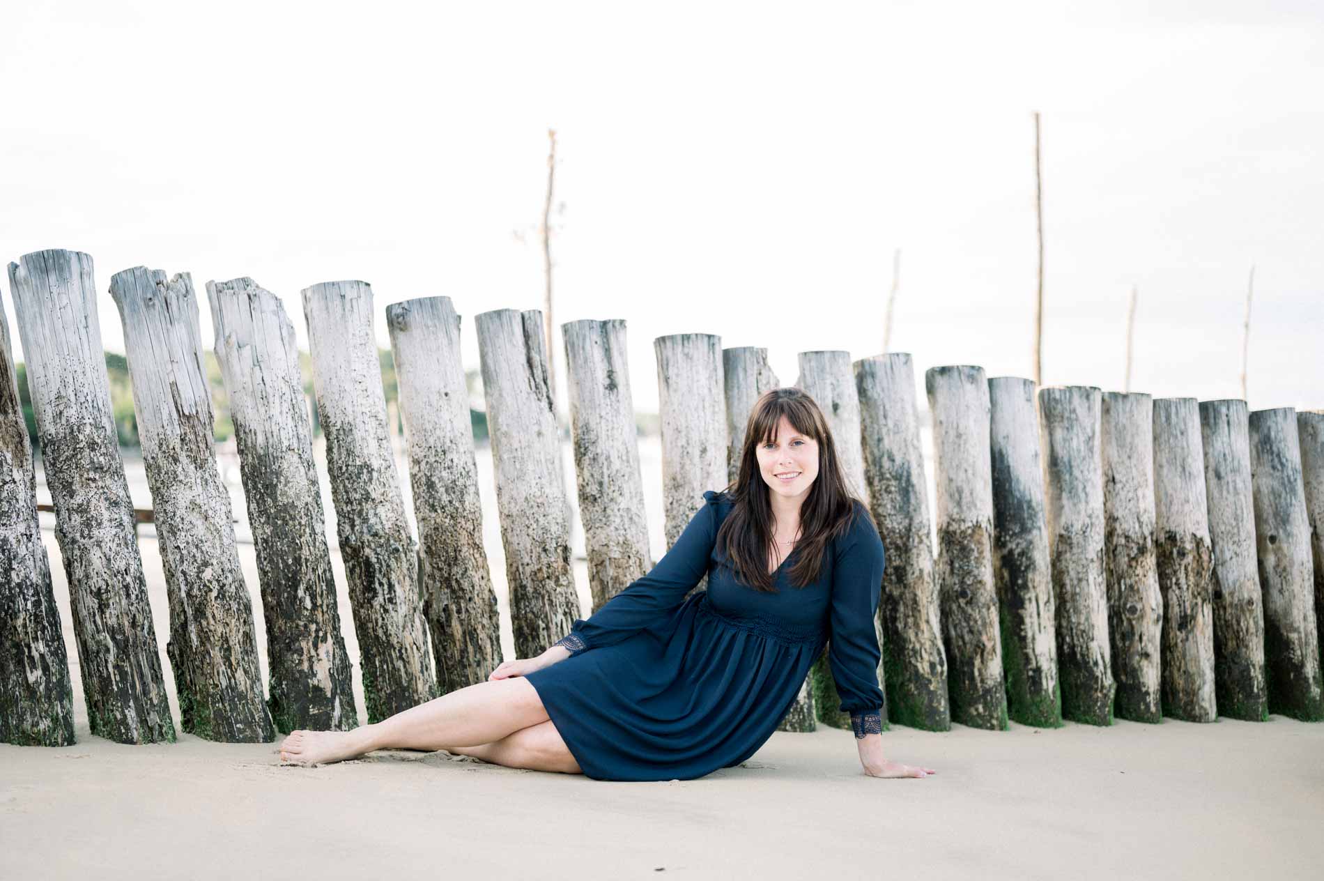 The bride-to-be lying on the sand in front of a row of wooden stakes