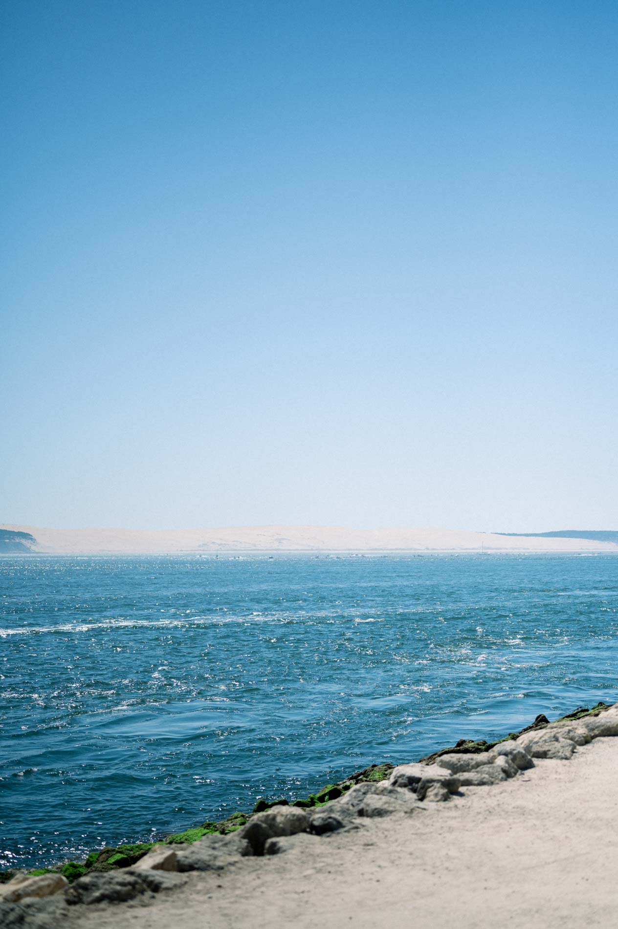 Blue water of the Arcachon Bay along a sea wall under a clear sky