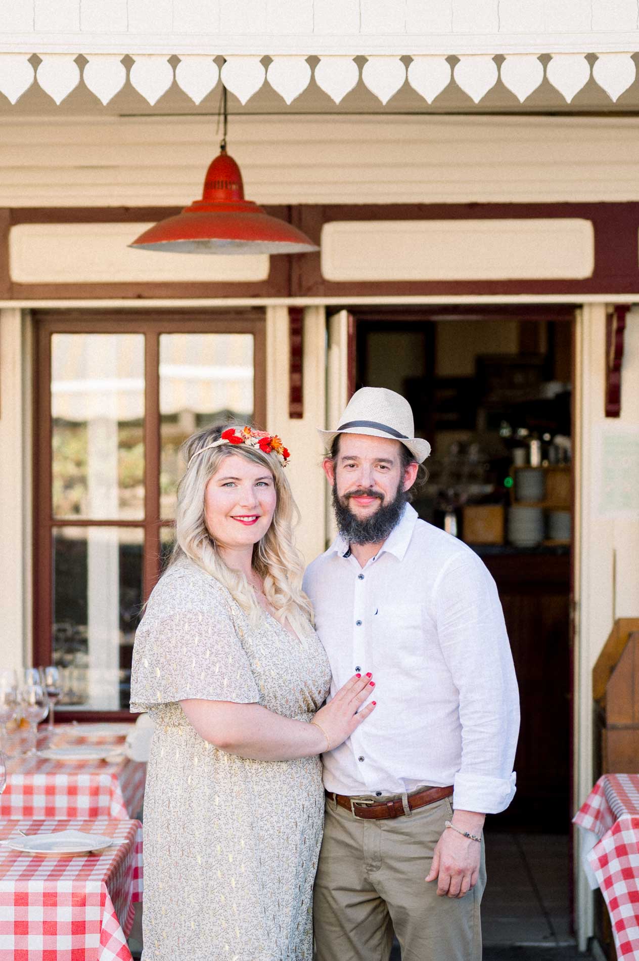 The couple standing in the doorway of a restaurant with red check tablecloths