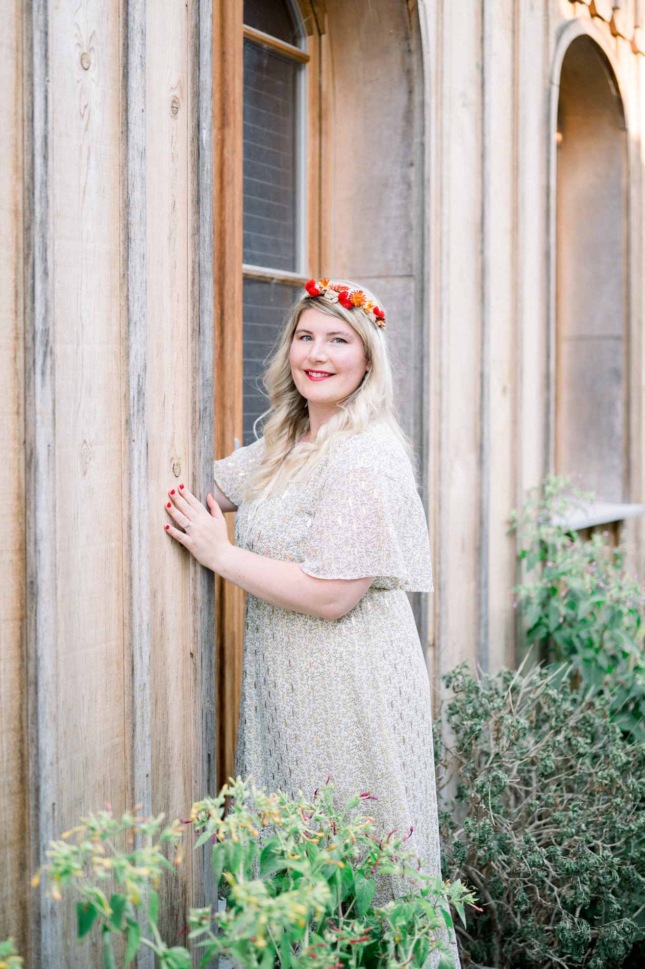 Woman in a flower crown leaning against a wooden cabin