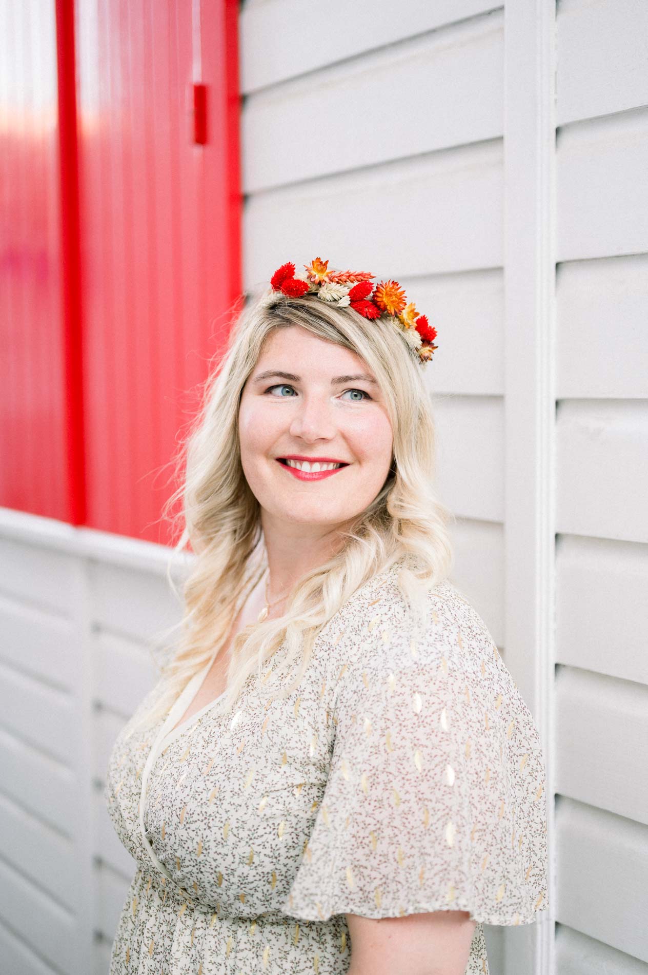 Smiling woman in a flower crown by a white cabin with red shutters