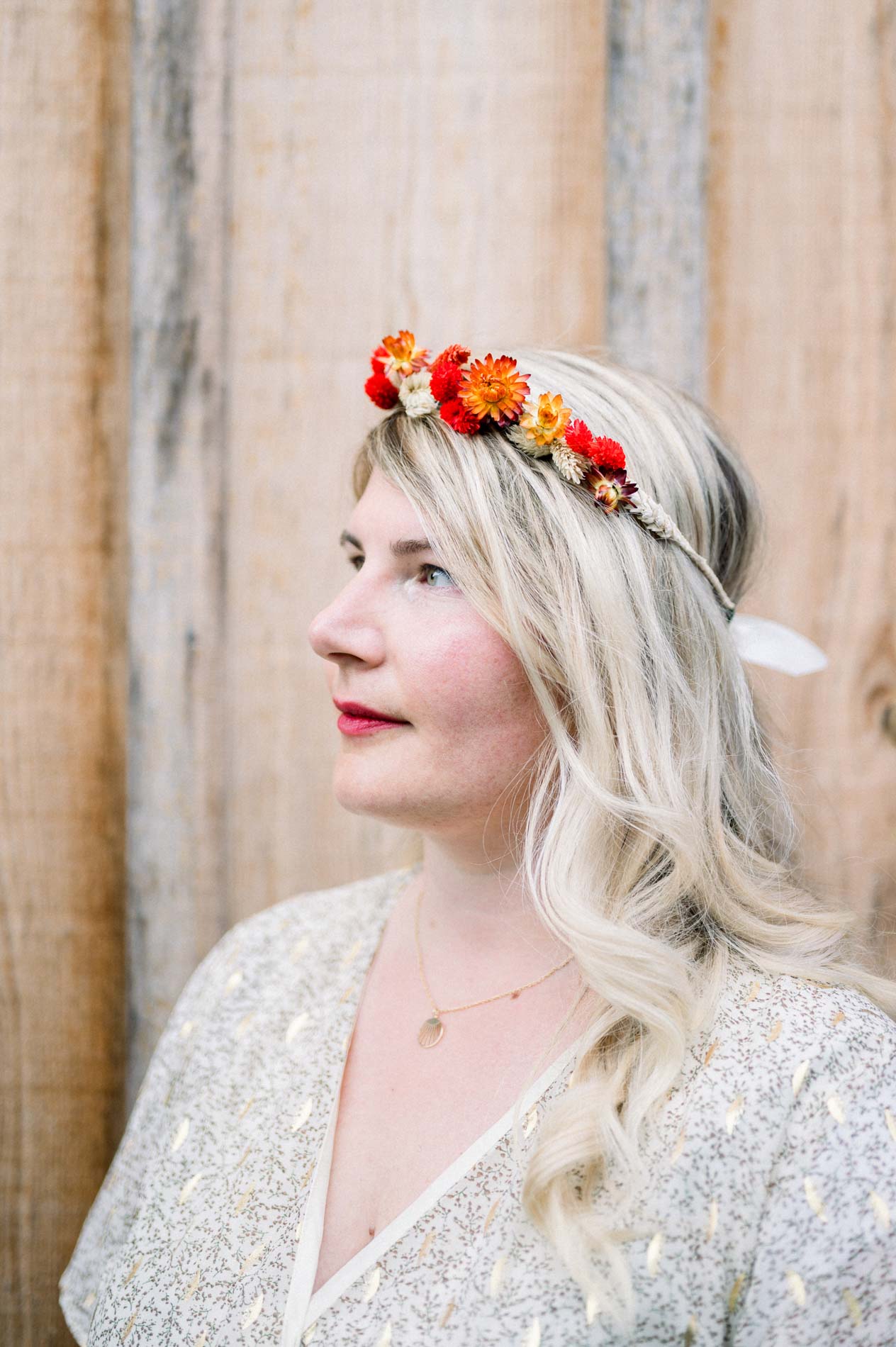 Profile of the woman in an orange flower crown against wooden cladding