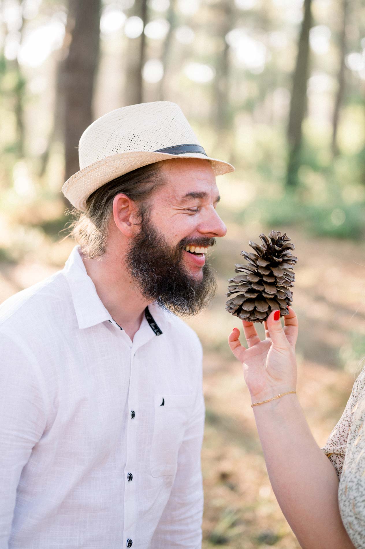 Man in a straw hat laughing at a pine cone held up to his face