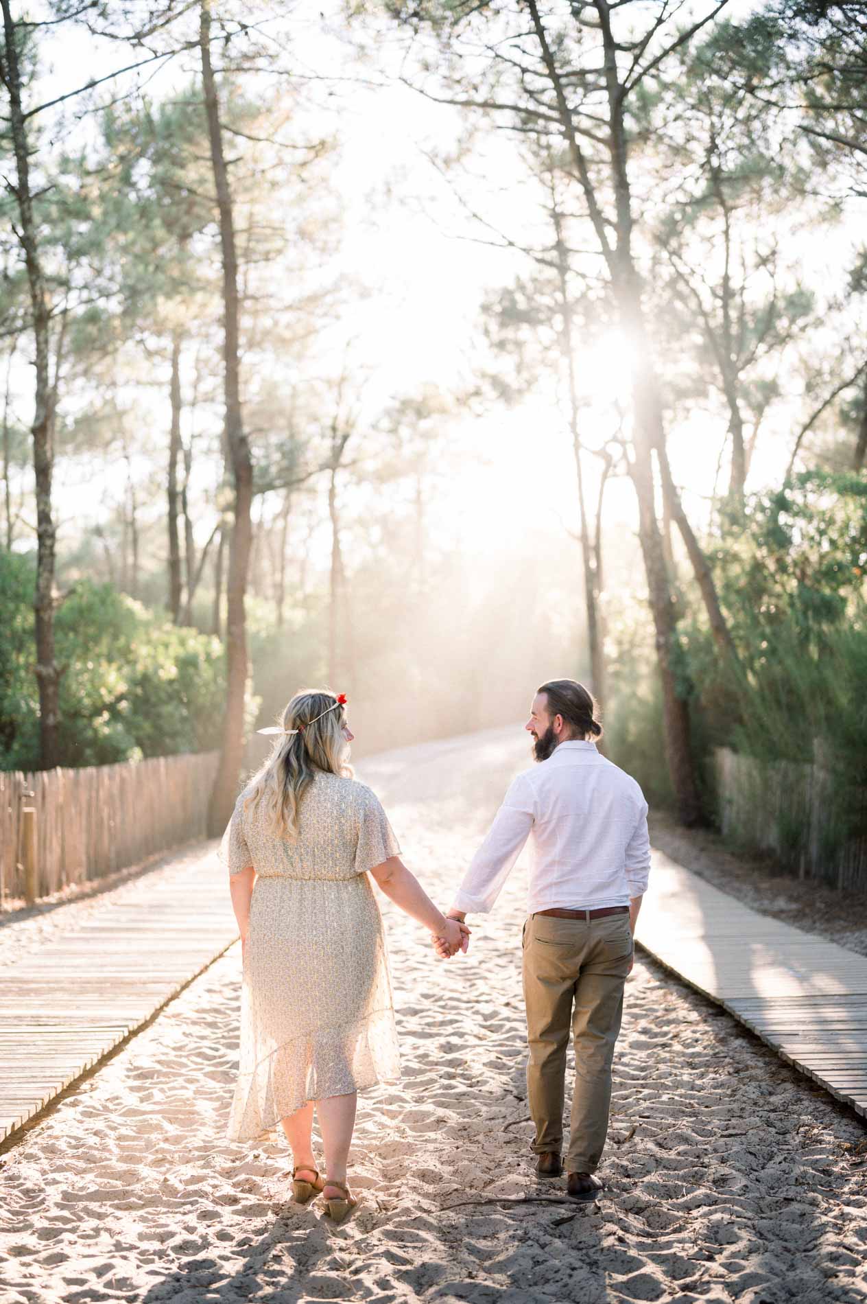 The couple walking hand in hand along a sandy path towards the beach