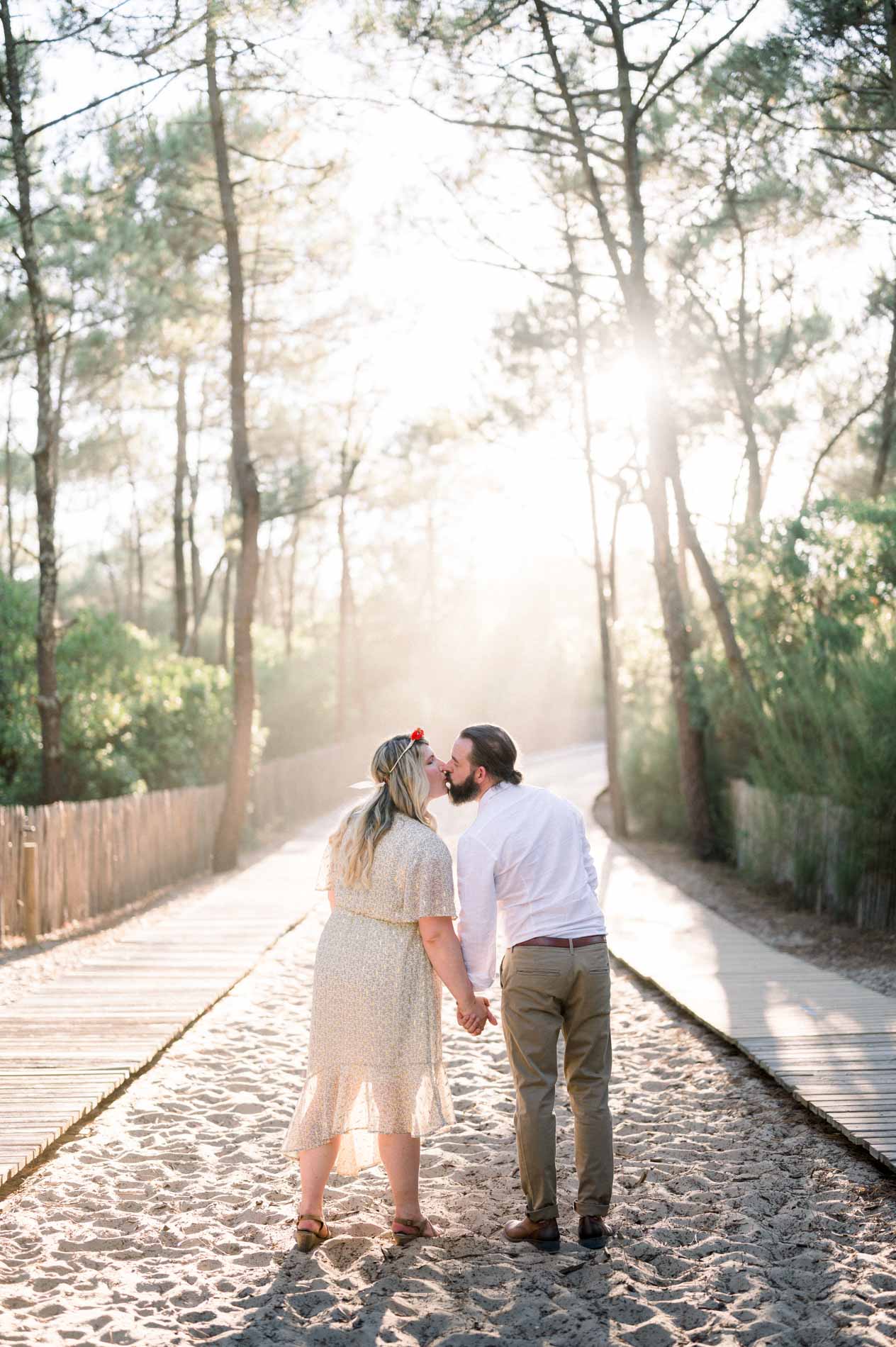 The couple kissing on the path to the beach, sun shining through the pines