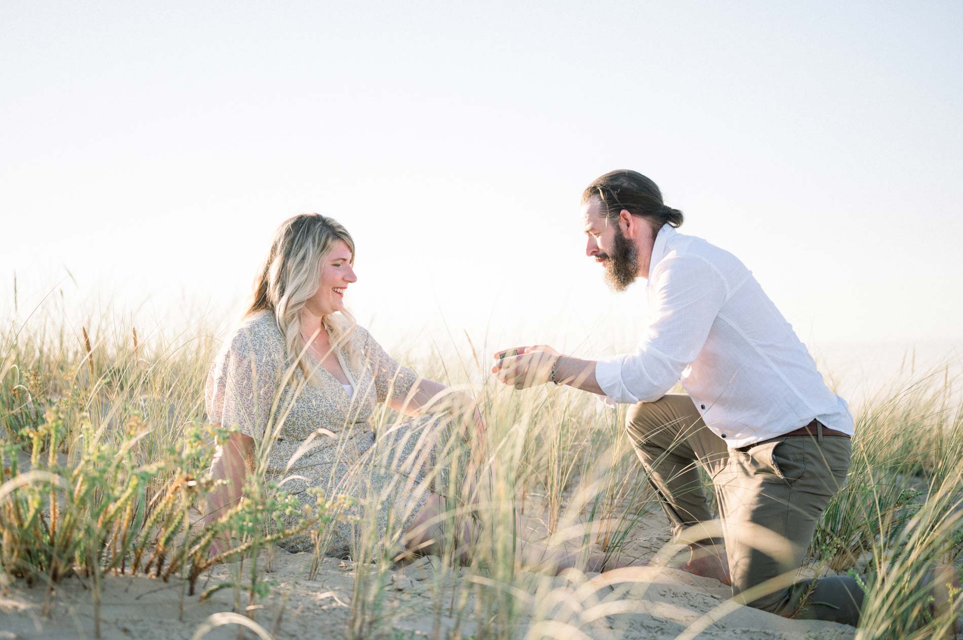 Derek down on one knee in the dunes proposing to Julie
