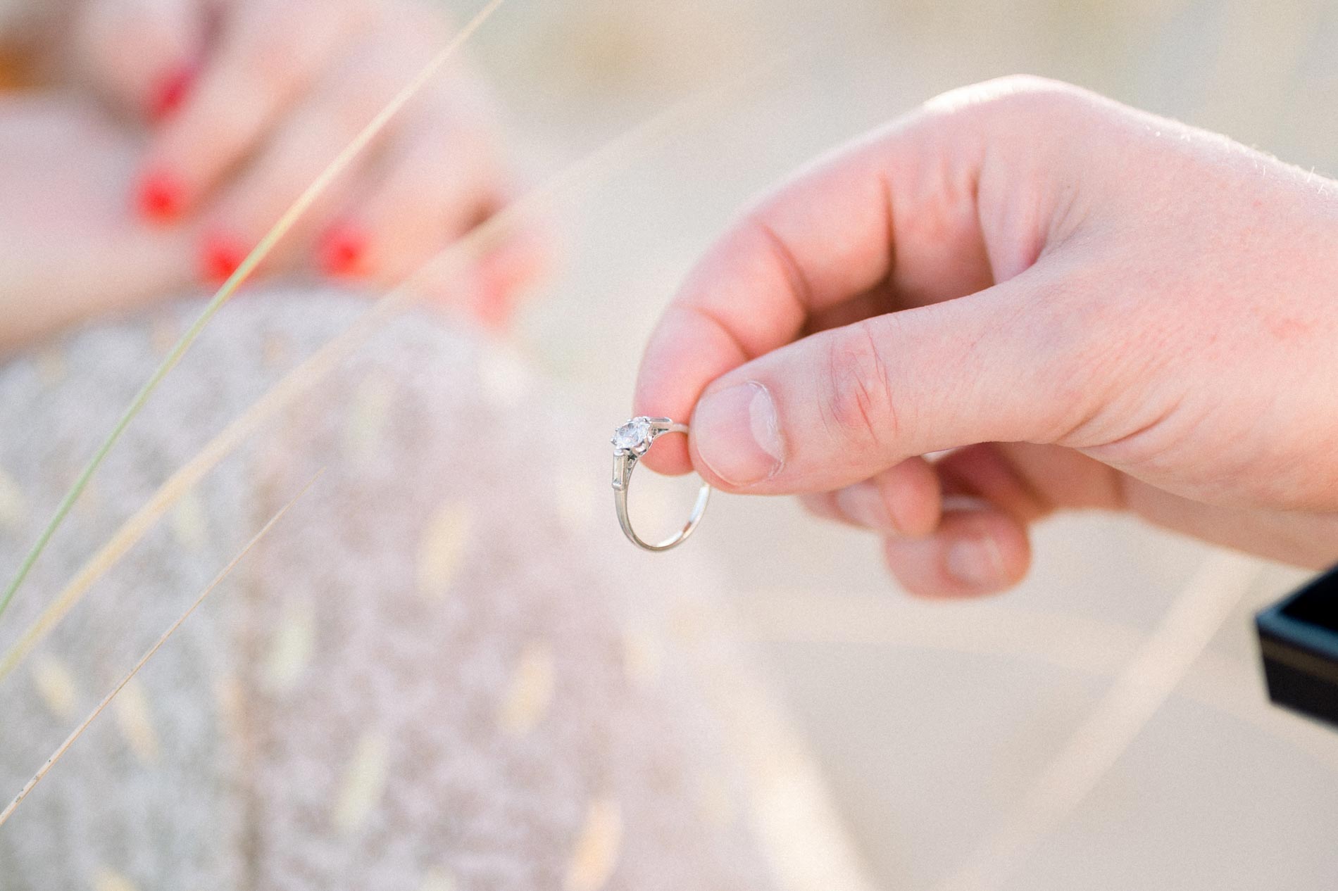 Derek holding out the engagement ring towards Julie's red-painted fingers
