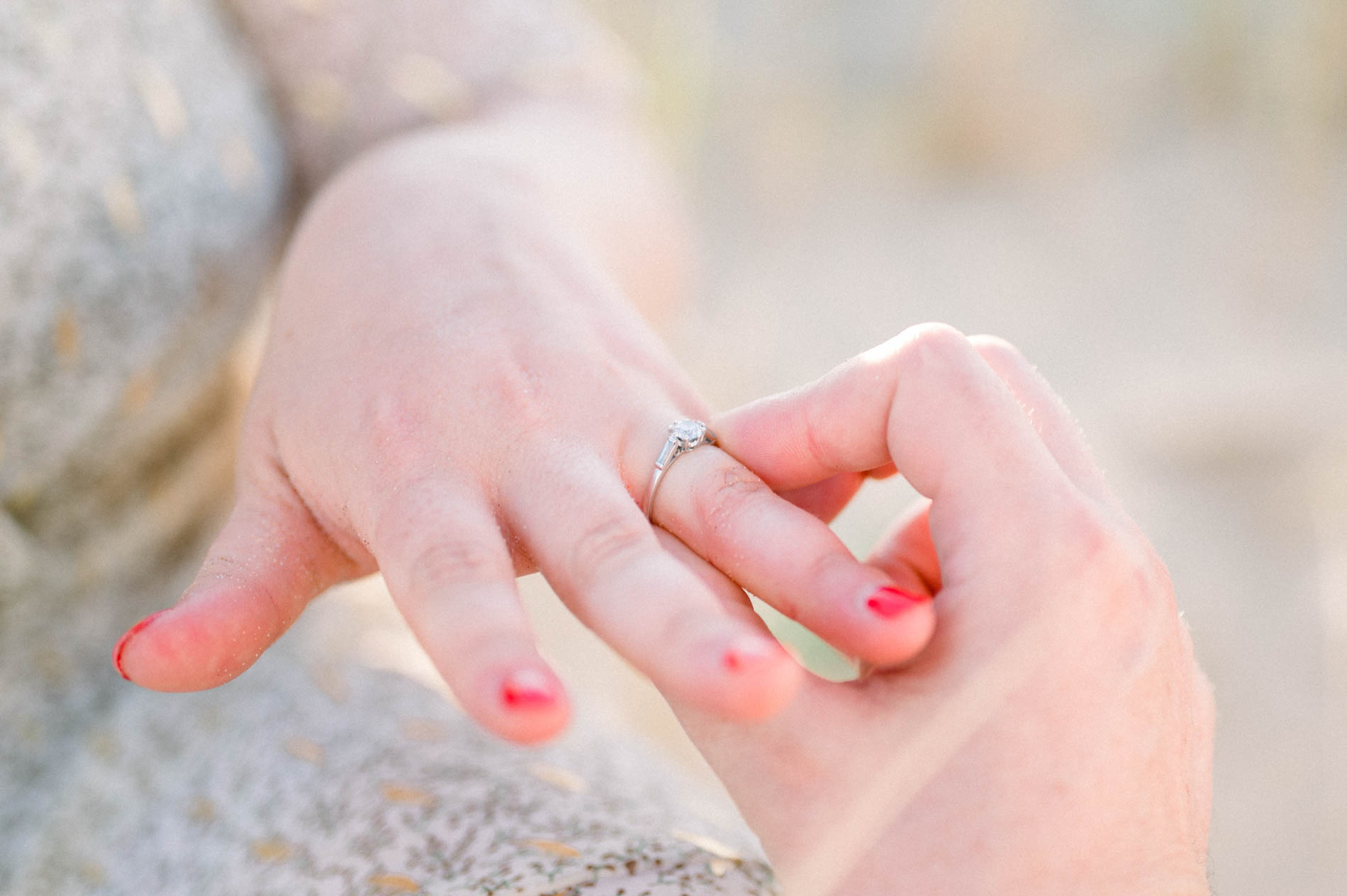 Close-up of the engagement ring slipped onto a finger with red nails