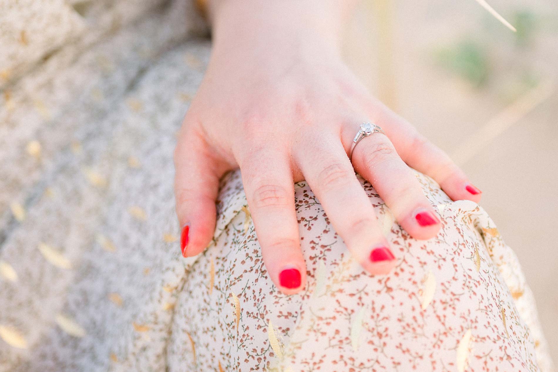 Ringed hand with red nails resting on a floral dress
