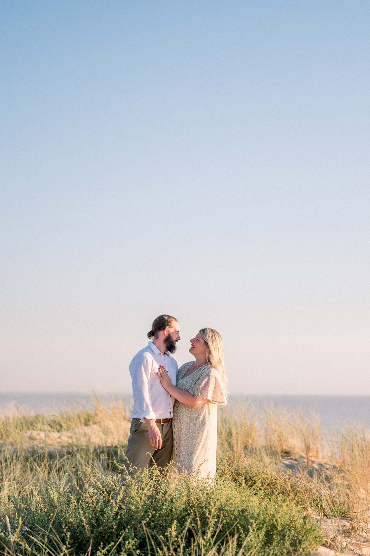 The newly engaged couple embracing on top of the dune facing the ocean