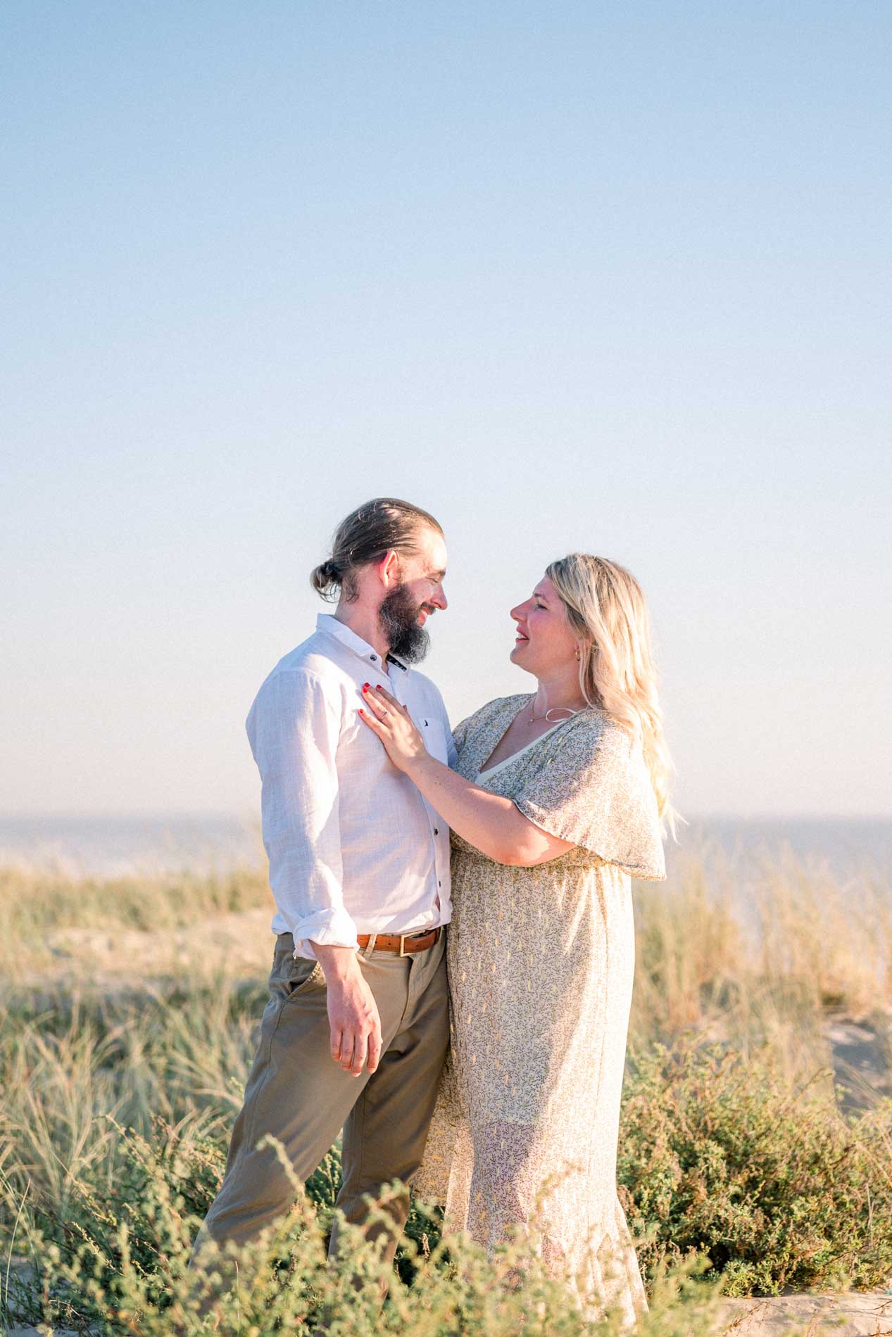 The smiling fiancés facing each other in the dune grass