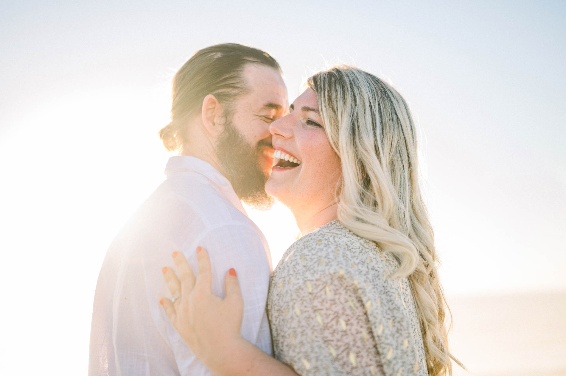 The fiancés laughing cheek to cheek in the setting sun