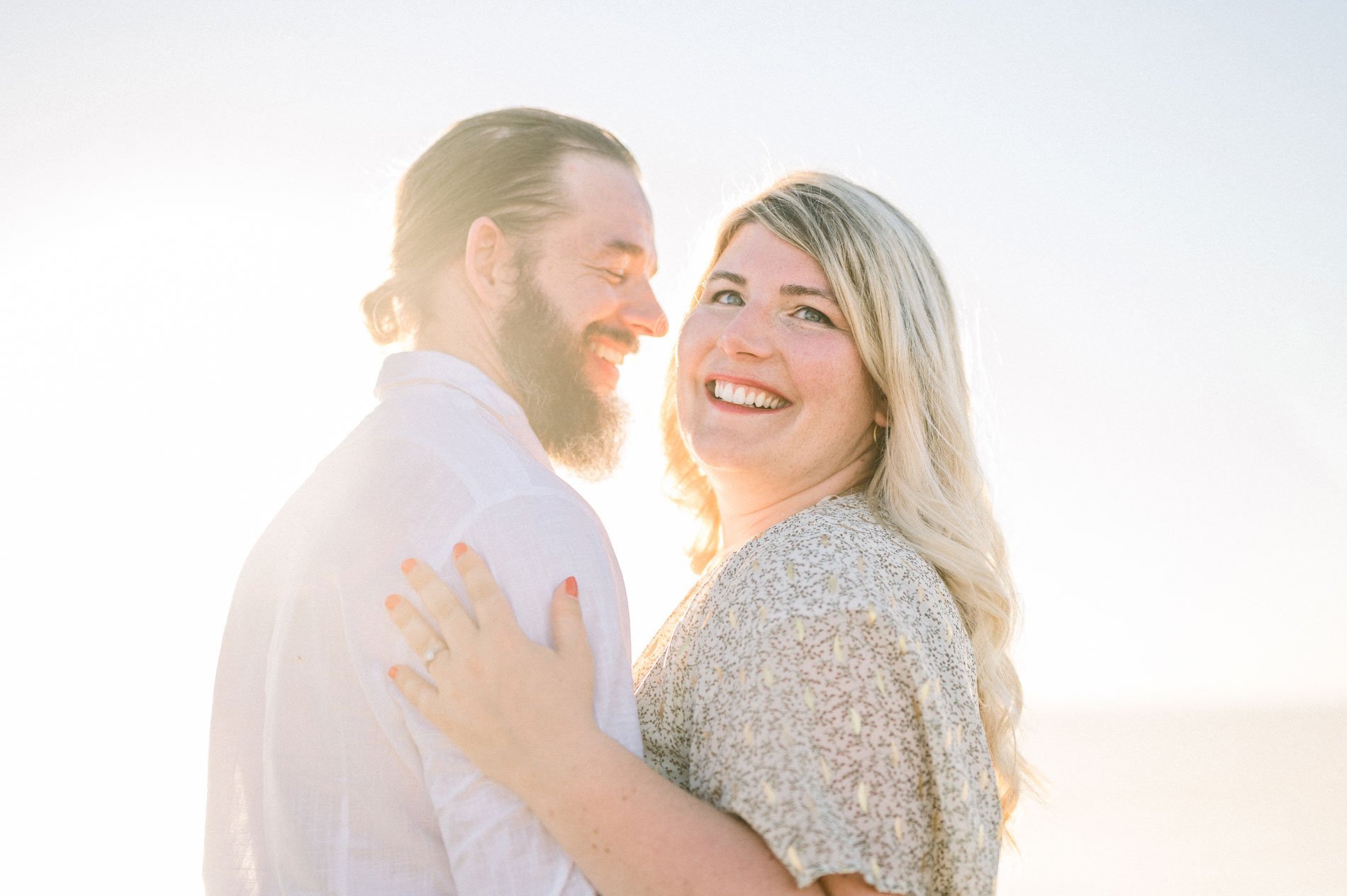 Julie smiling at the camera, nestled against Derek at sunset